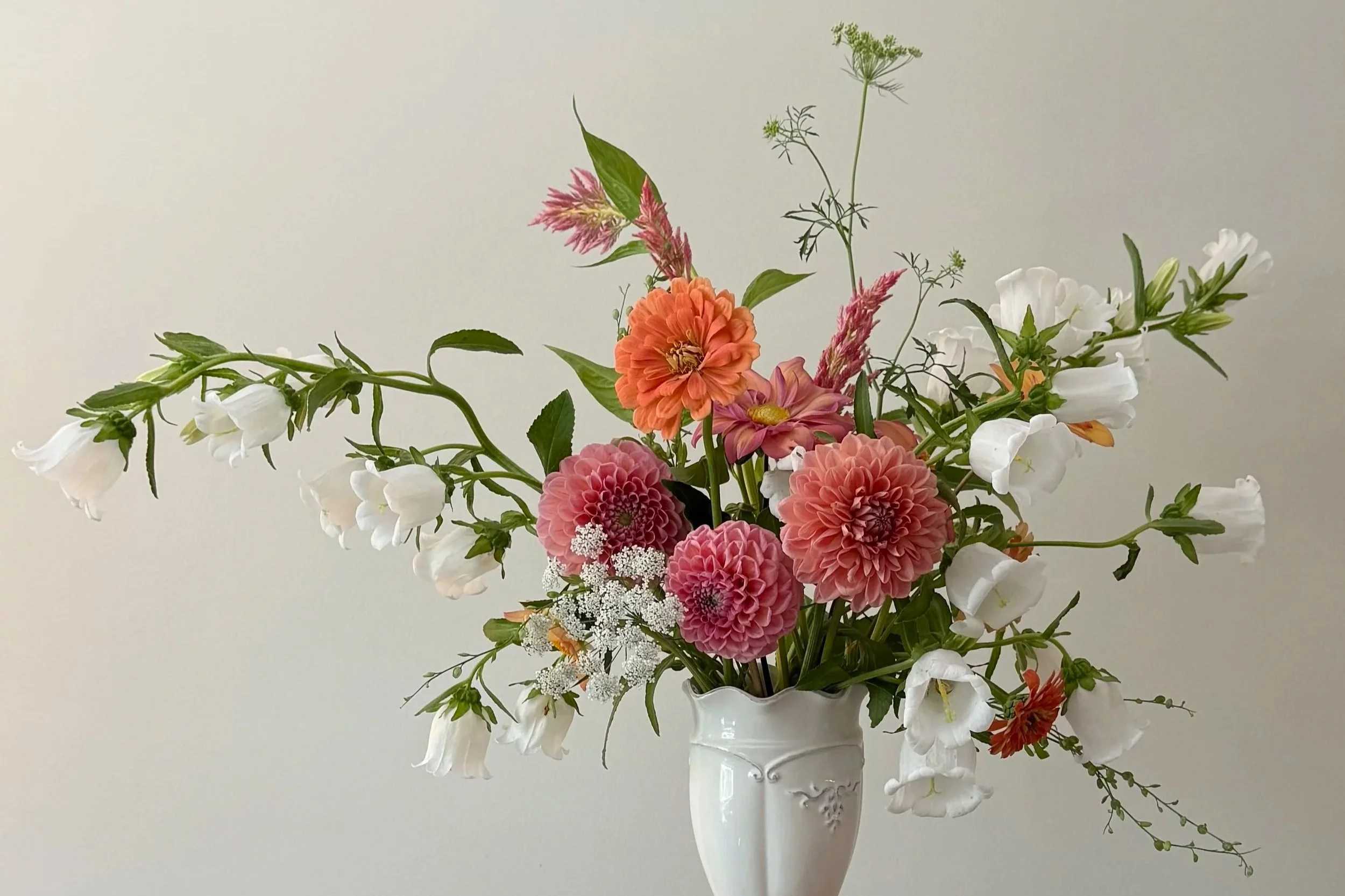 flower arrangement with peach, pink, and white flowers in a white vase
