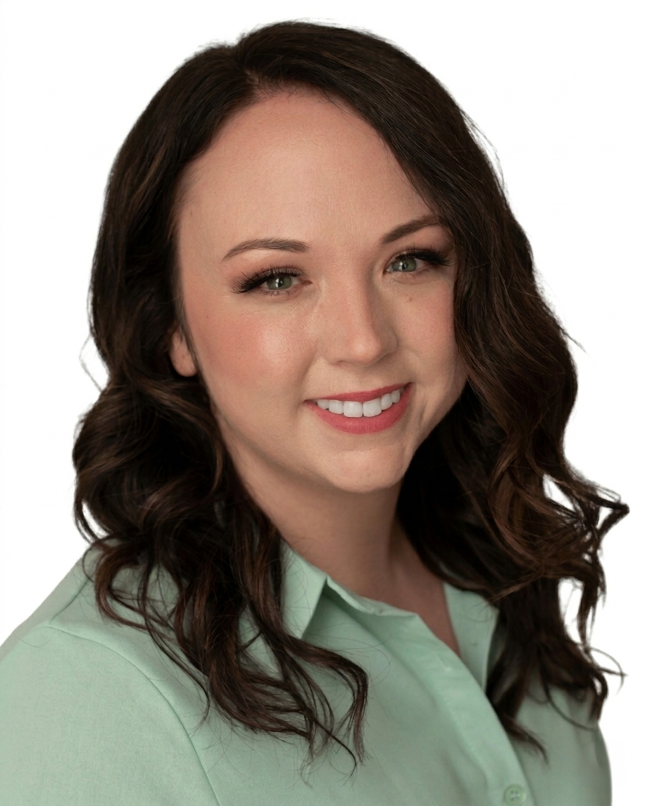A young woman with shoulder-length wavy brown hair, fair skin, green eyes, and makeup, smiling at the camera, wearing a light green collared shirt.
