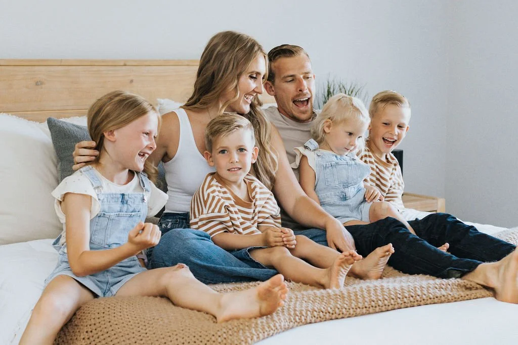 Family sitting on a bed together, smiling and laughing.