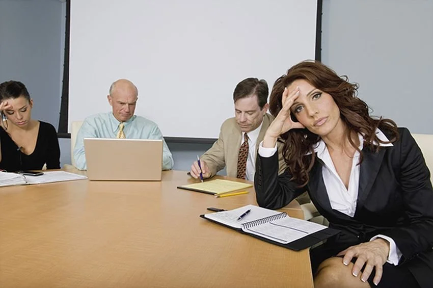 Business meeting with four people at a conference table, the woman on the right appears stressed or overwhelmed.