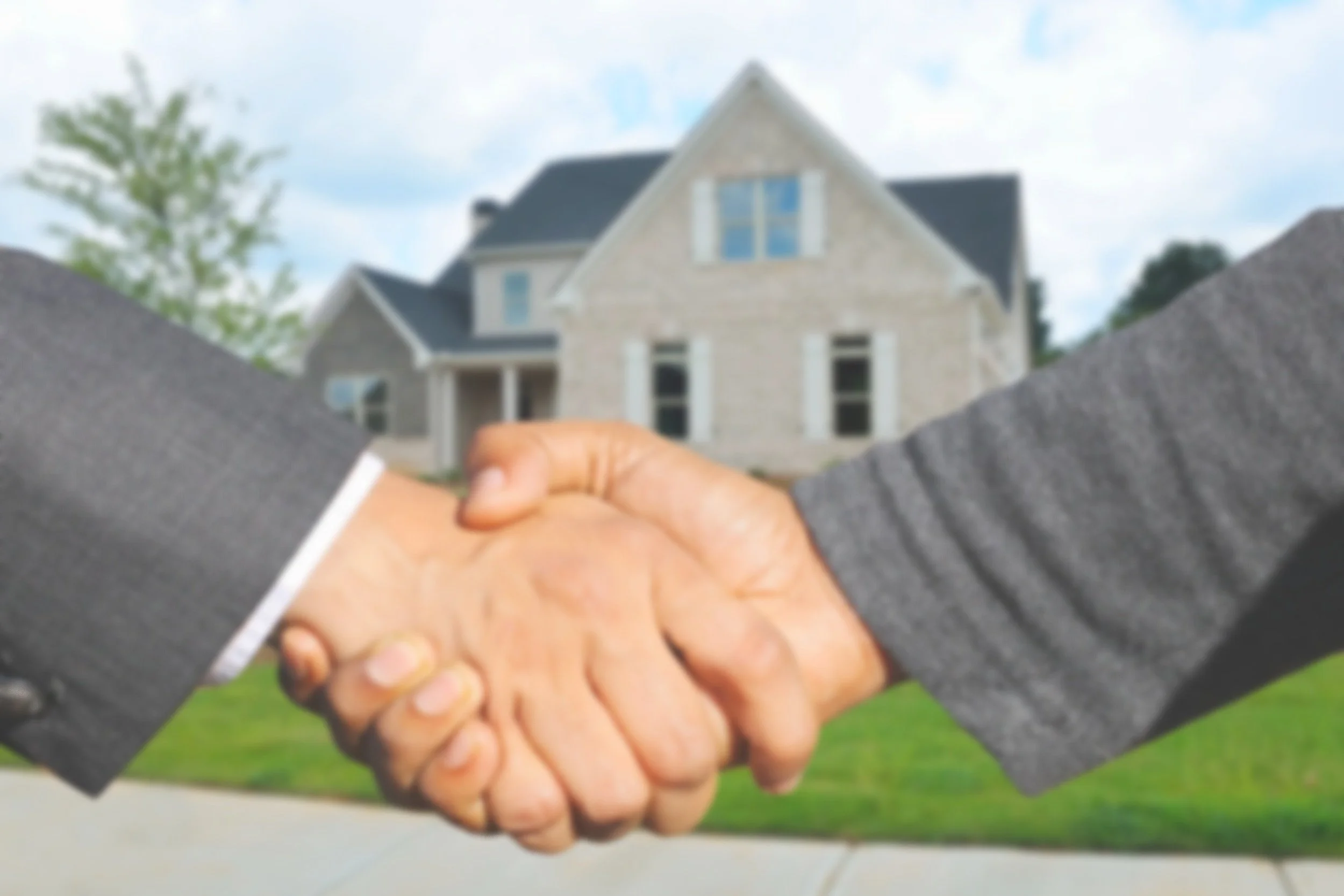 A close-up of two people shaking hands in front of a house, symbolizing a real estate transaction.