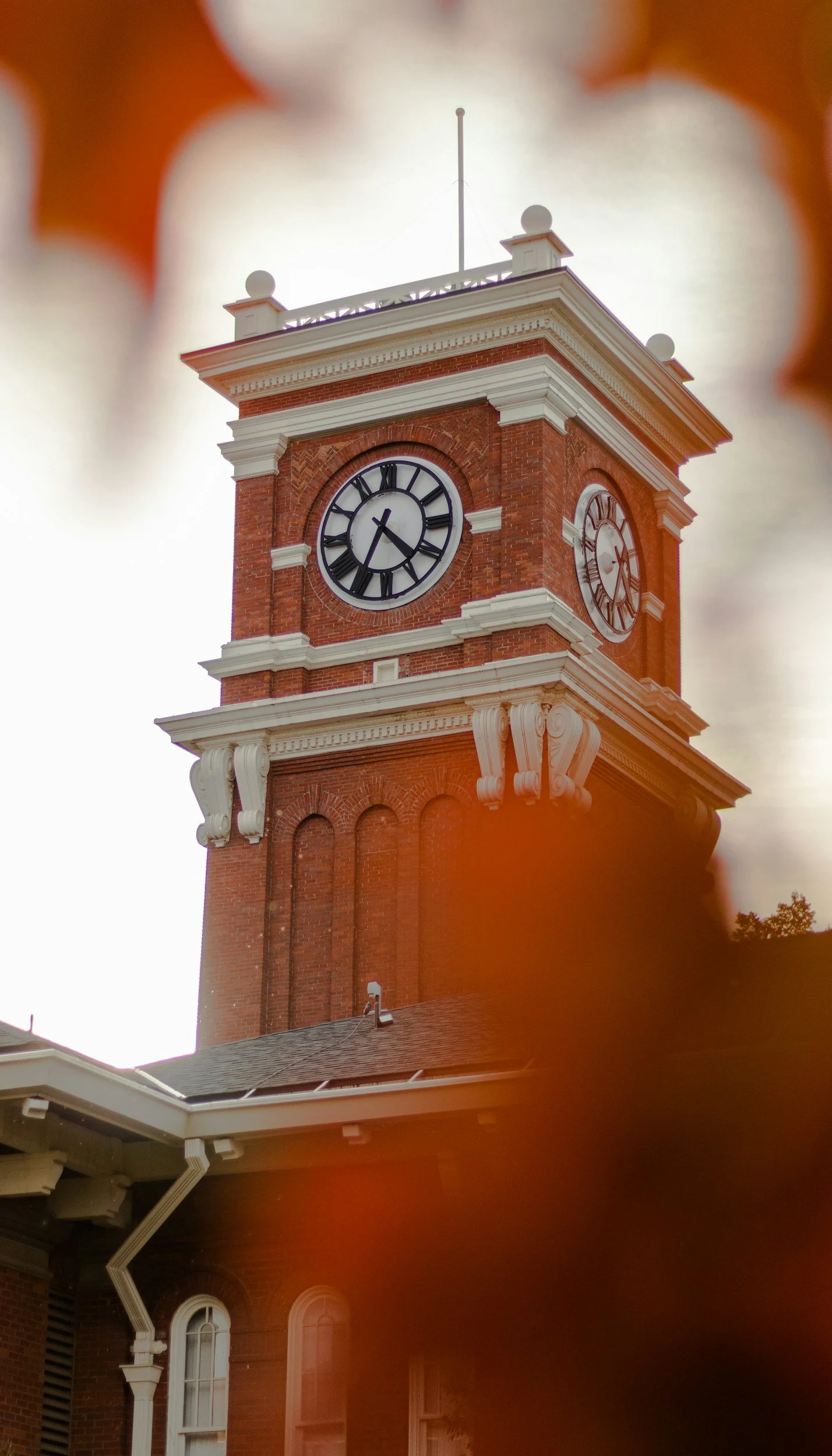 Historic brick clock tower with white accents, two clock faces showing the time, and a flagpole on top, seen through an orange-brownish out-of-focus border.