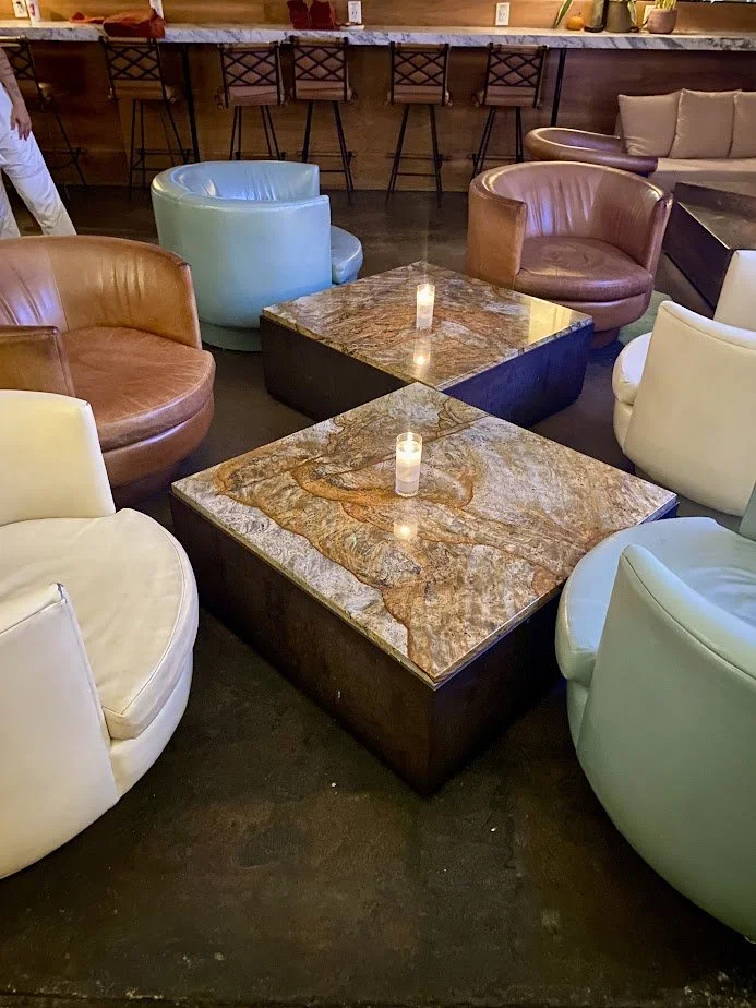 Several round, leather lounge chairs in various colors surrounding two square, marble-top coffee tables with candles, in a cozy indoor setting.