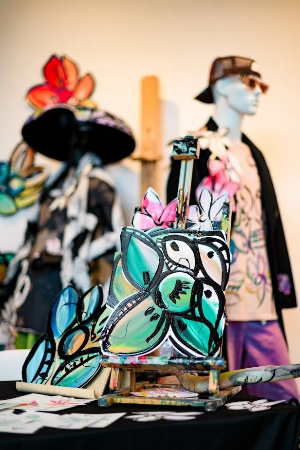 Display of colorful butterfly-shaped stained glass art and mannequins dressed in tropical-themed clothing at an art market or boutique.