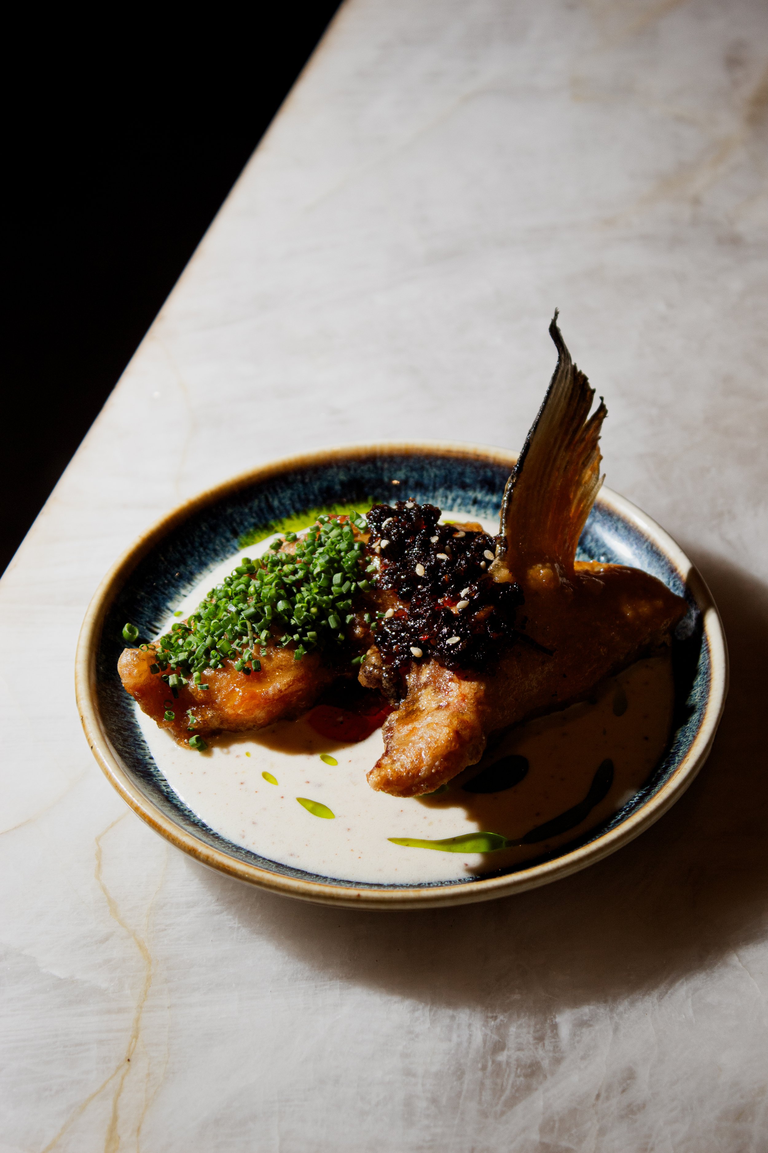 A Japanese classic reinterpreted — crispy salmon kama with smooth cream, salsa macha, and fresh herbs at REMU Tulum.