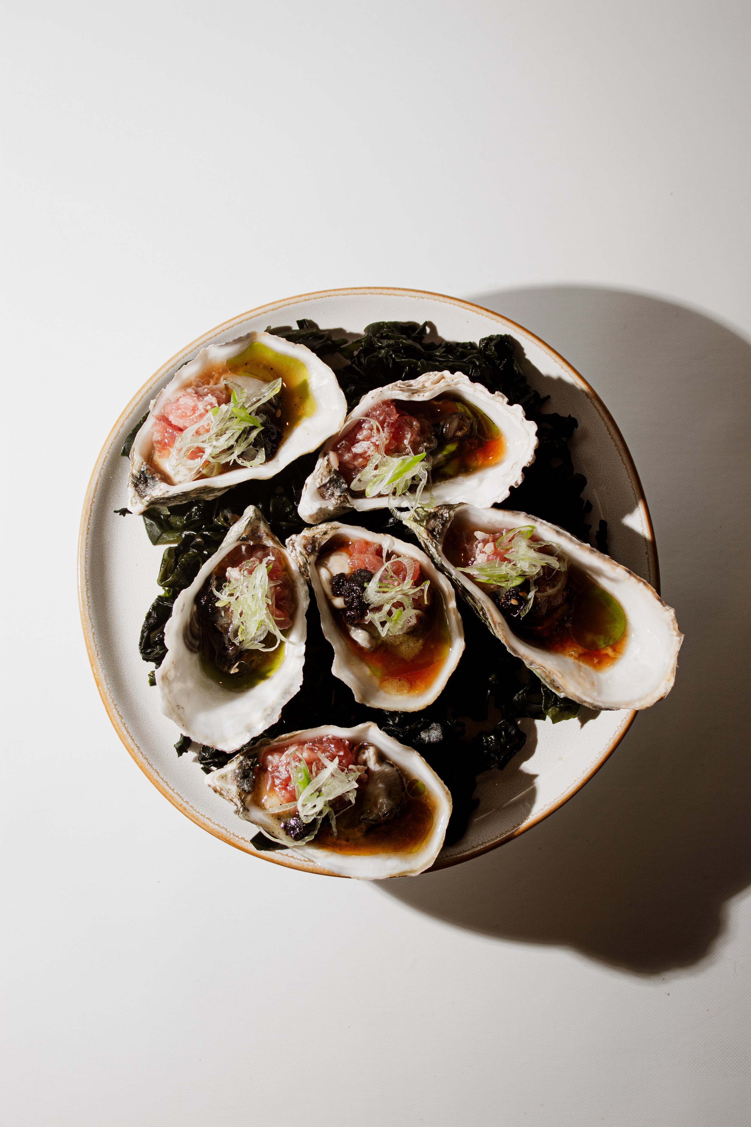 Fresh oysters topped with bluefin tuna tartare, ponzu, salsa macha, and crispy sexy onion, served over seaweed at REMU Matcha & Sushi Bar in Tulum.