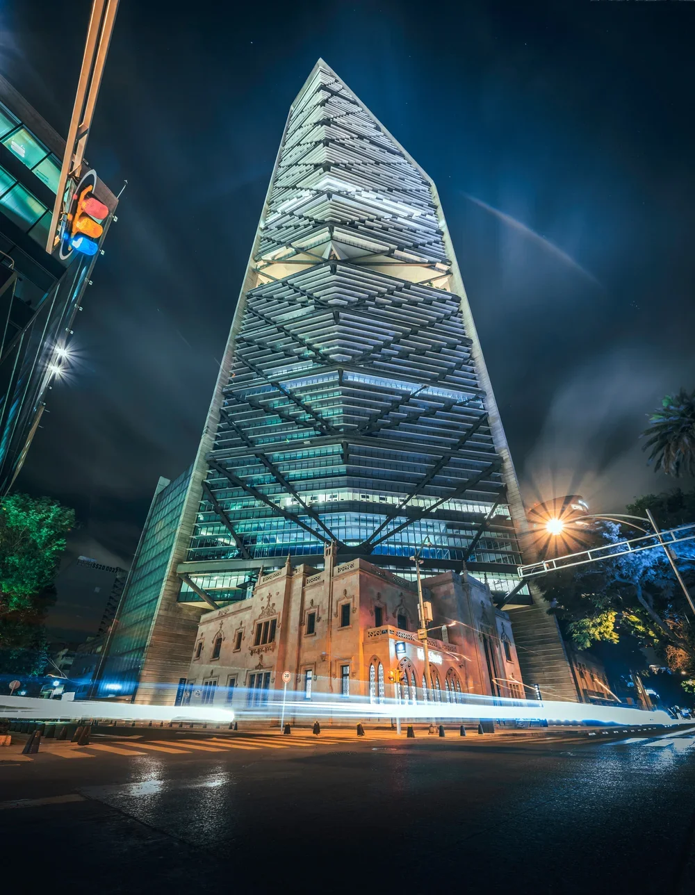 Edificio alto y moderno en la noche, con luces brillantes y tráfico en primer plano, en una ciudad urbana.