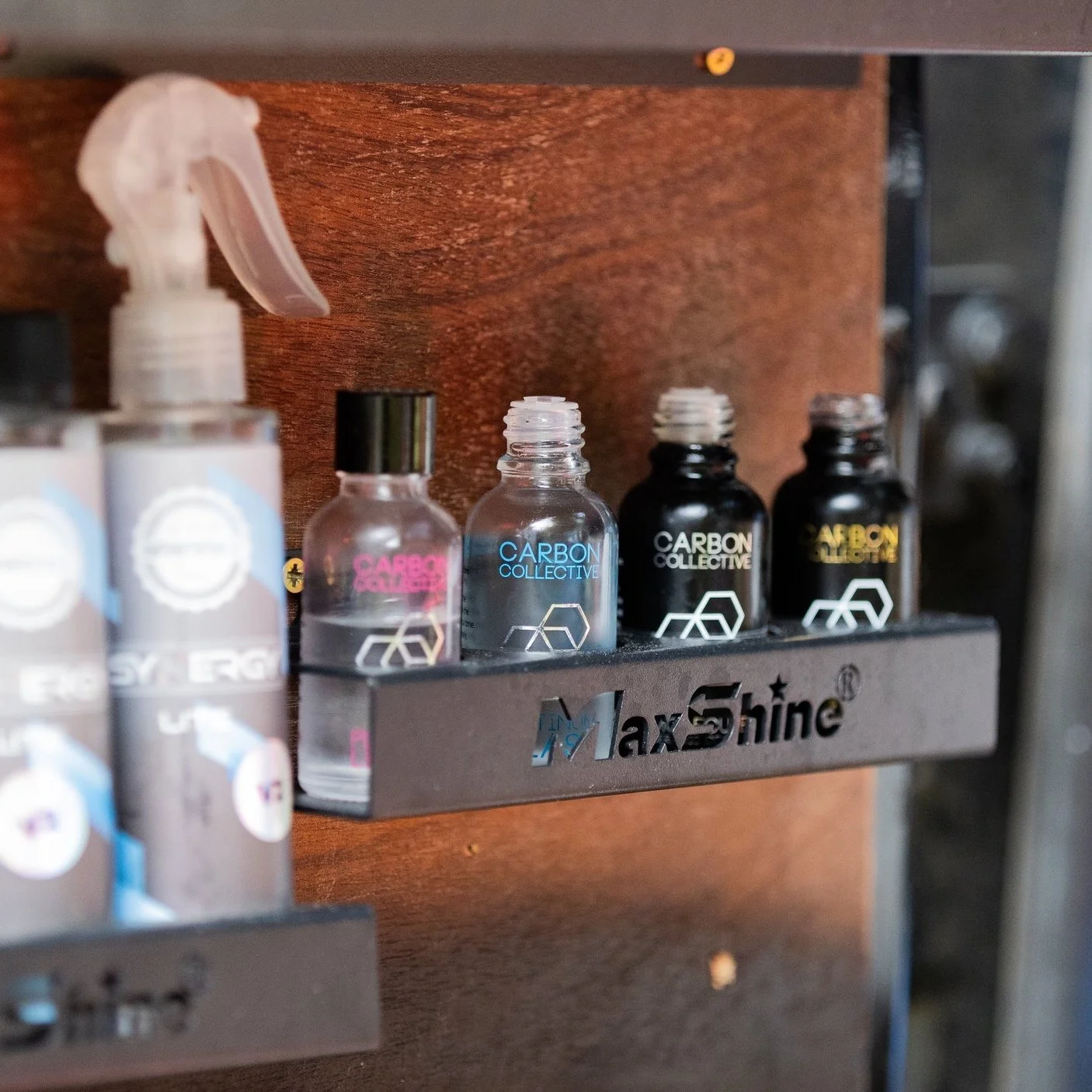 Small bottles of Carbon Collective e-liquid or vape juice placed on a black metal shelf with the MaxShine logo, mounted on a wooden surface.