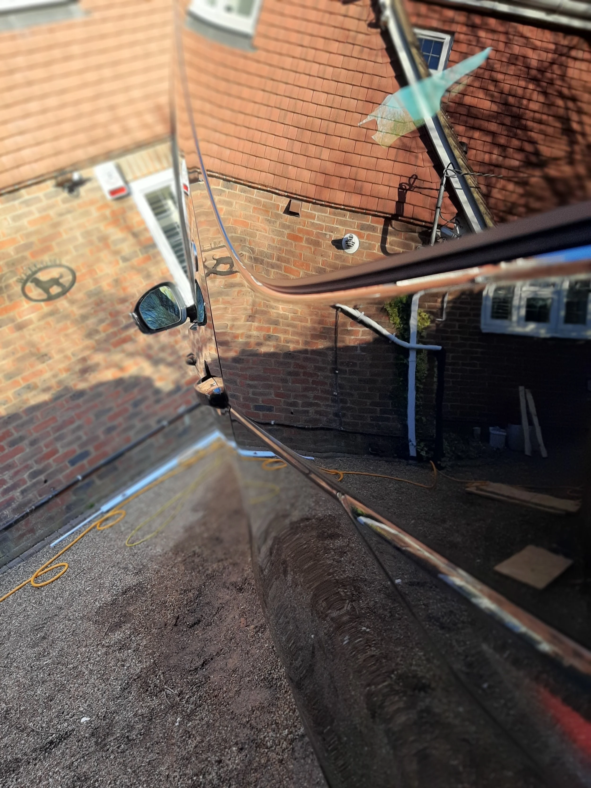 Reflection of a brick house and objects on the ground in a car's shiny black door.