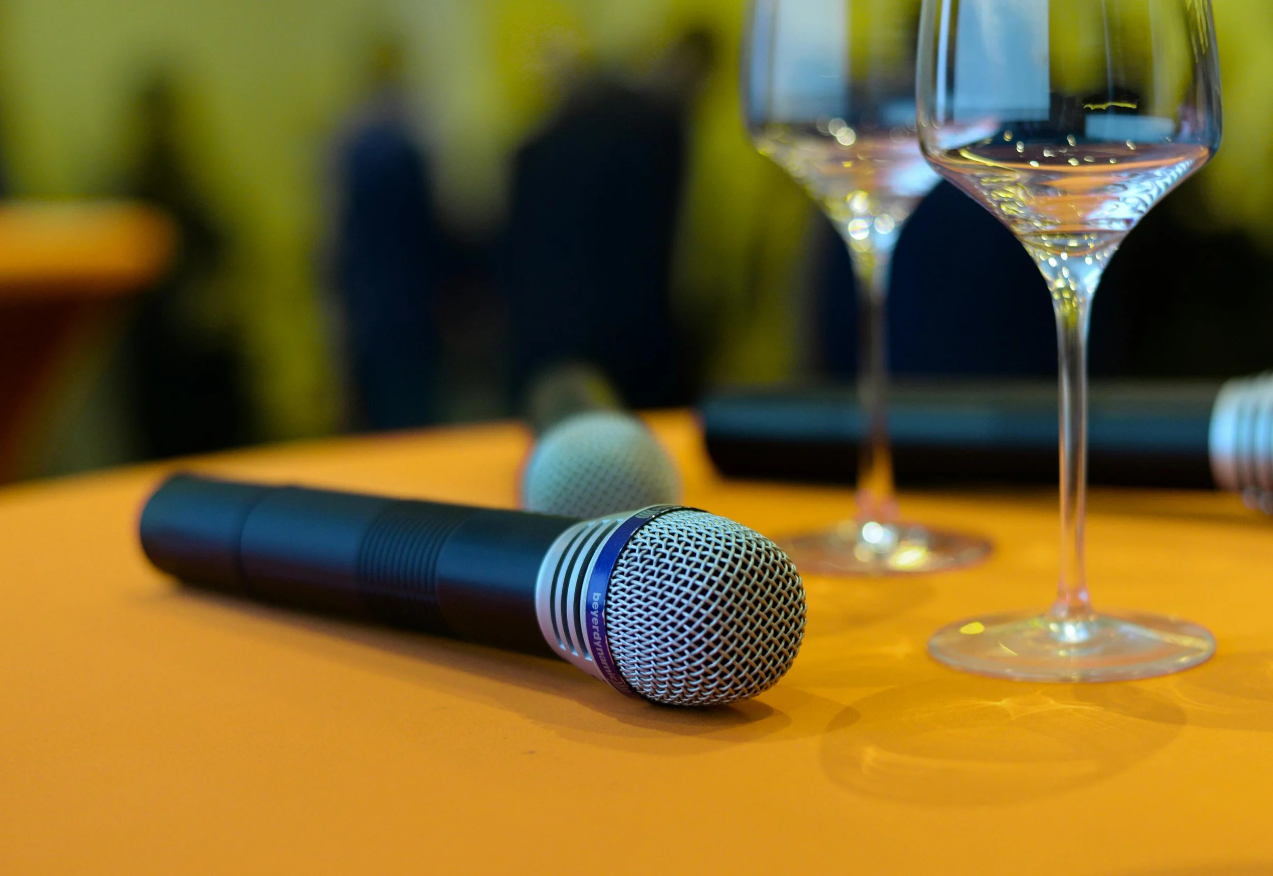 Microphone lying on a wooden table with a wine glass and blurred background.