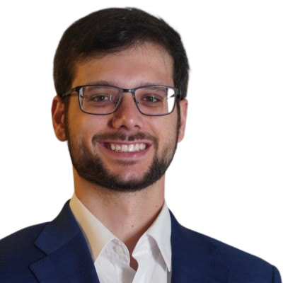 A man with dark hair, glasses, and a beard, smiling, wearing a navy blazer and white shirt.