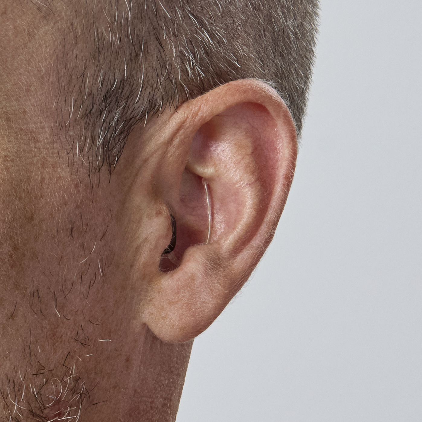 Close-up of a person's ear with a thin, transparent hearing aid wire.