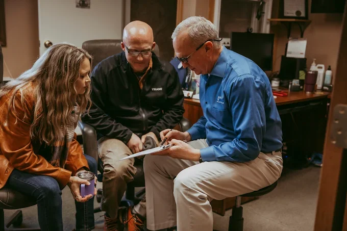 Three people sitting around discussing documents in an office setting.