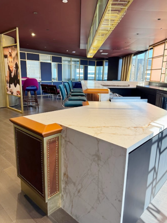 Empty modern interior with a marble-topped bar counter and teal chairs stacked in a room with large windows and city view.