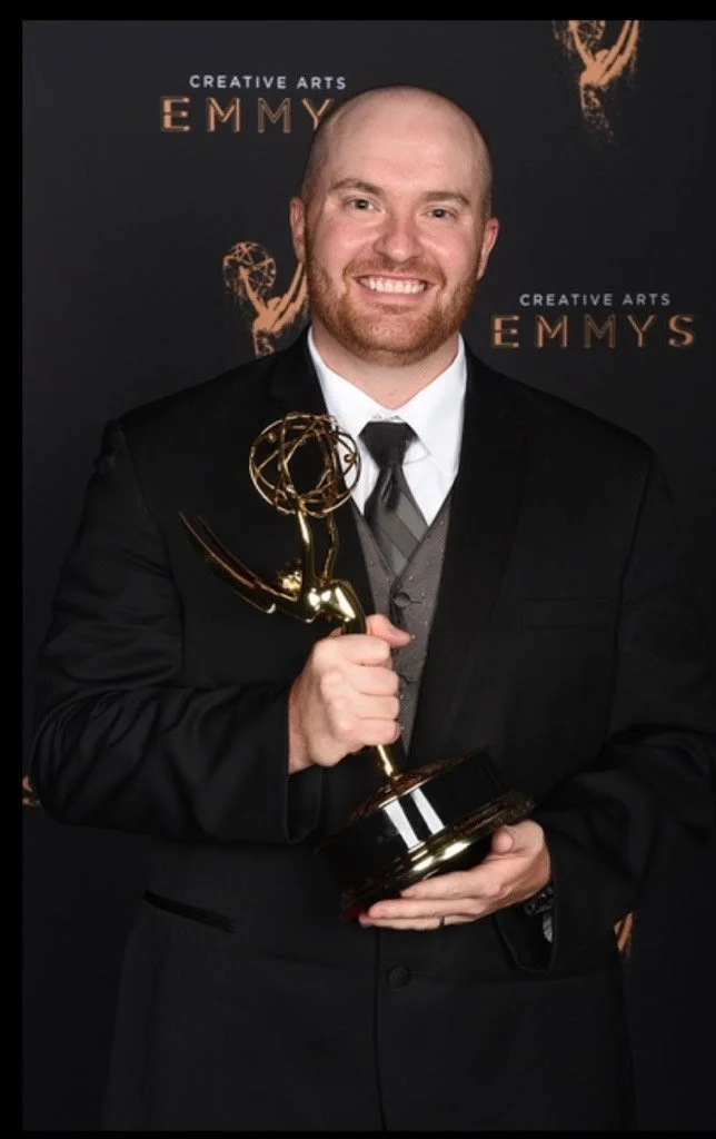 A man in a suit holding an Emmy award trophy at the Creative Arts Emmy Awards.