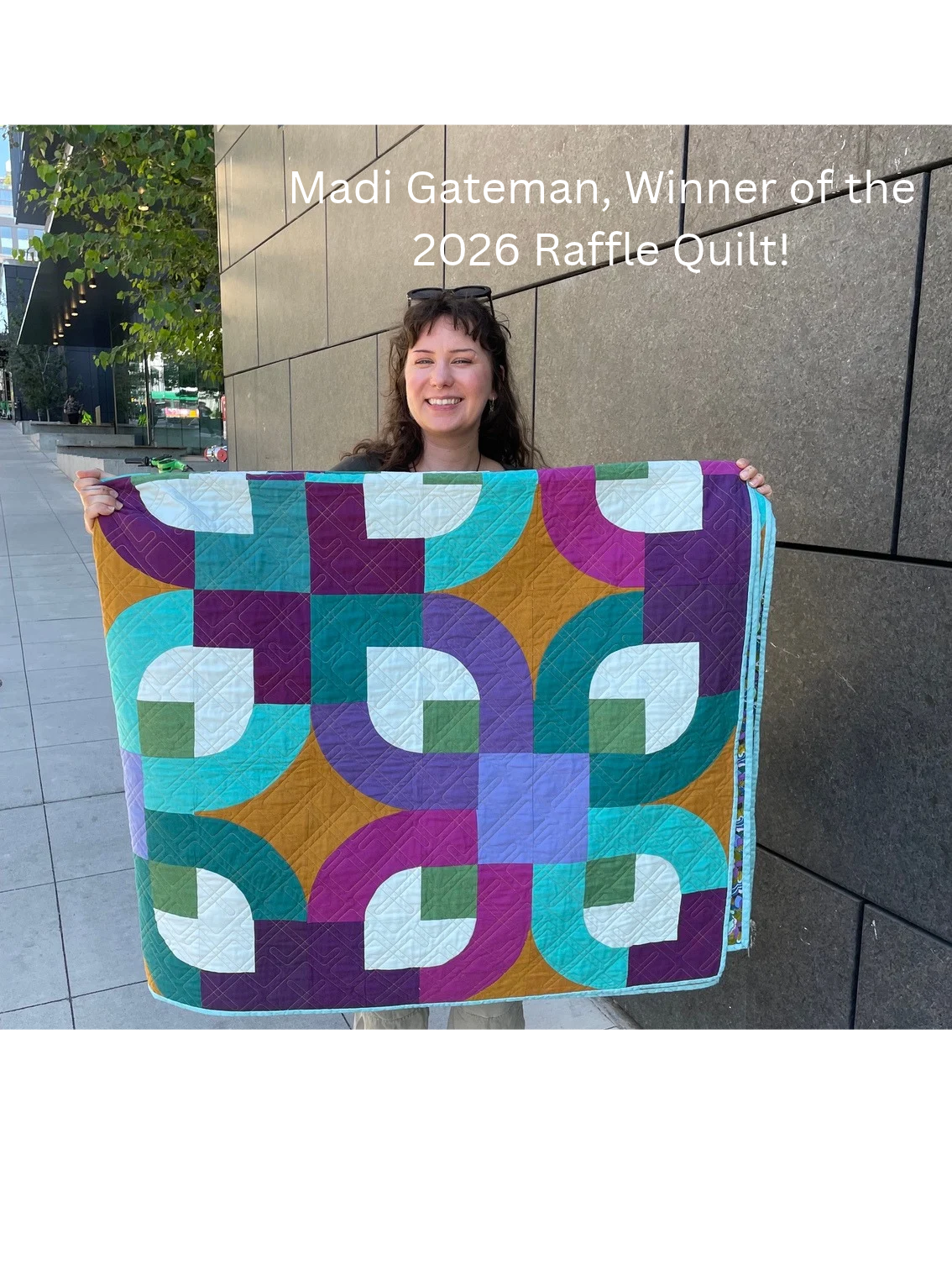 woman smiling with a folded quilt held out in front of her.