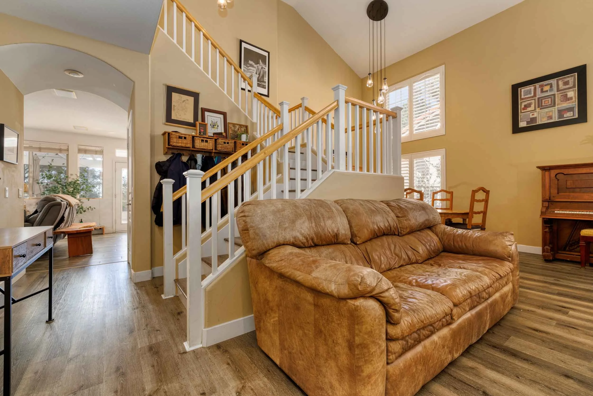 Professional real estate interior photo by Half Full Real Estate Photography — vaulted living room with open staircase, hardwood floors, upright piano, and arched entryway to front door.