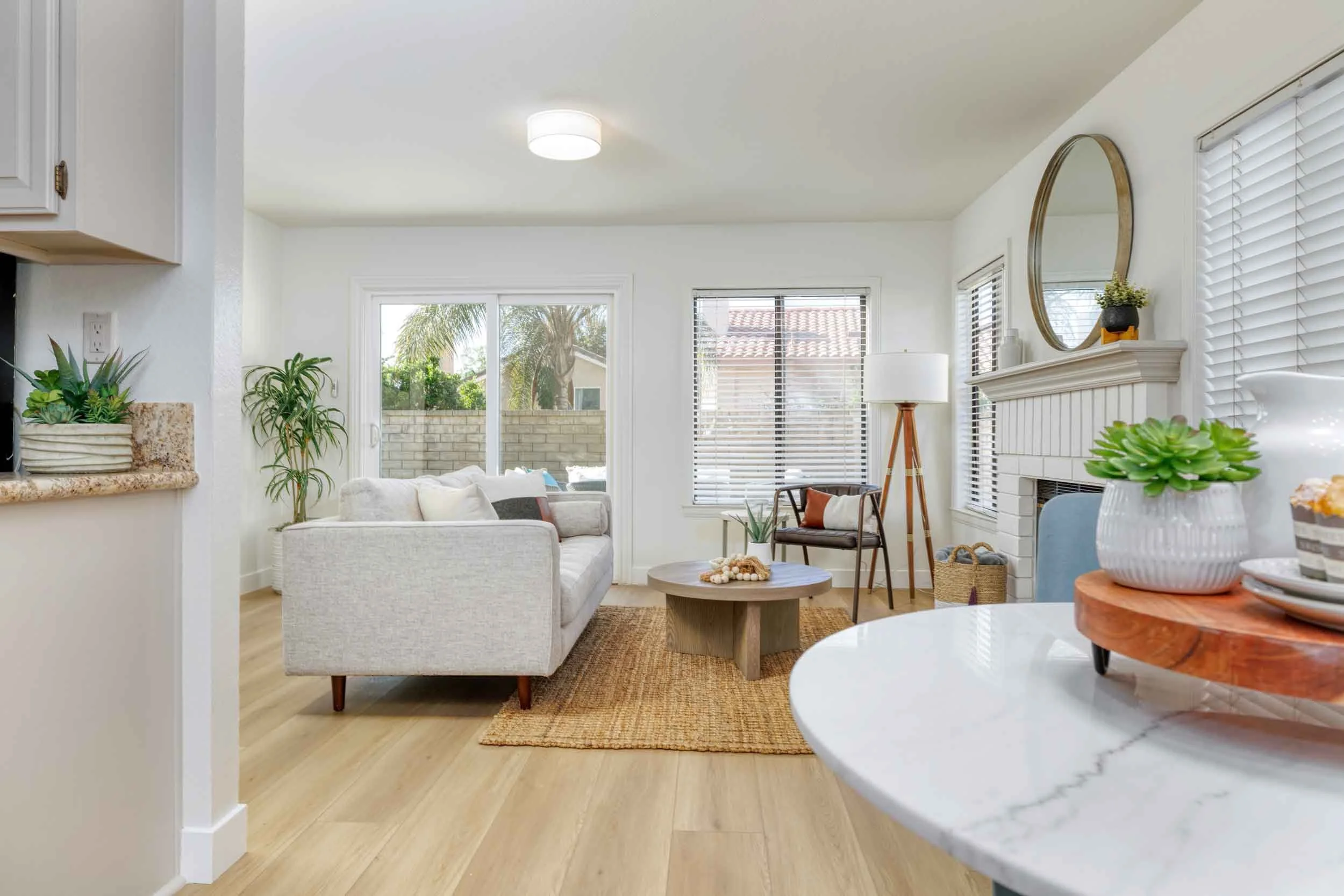 Professional real estate interior photo by Half Full Real Estate Photography — bright living and dining area with light wood floors, white tile fireplace, jute rug, and sliding glass door to patio.