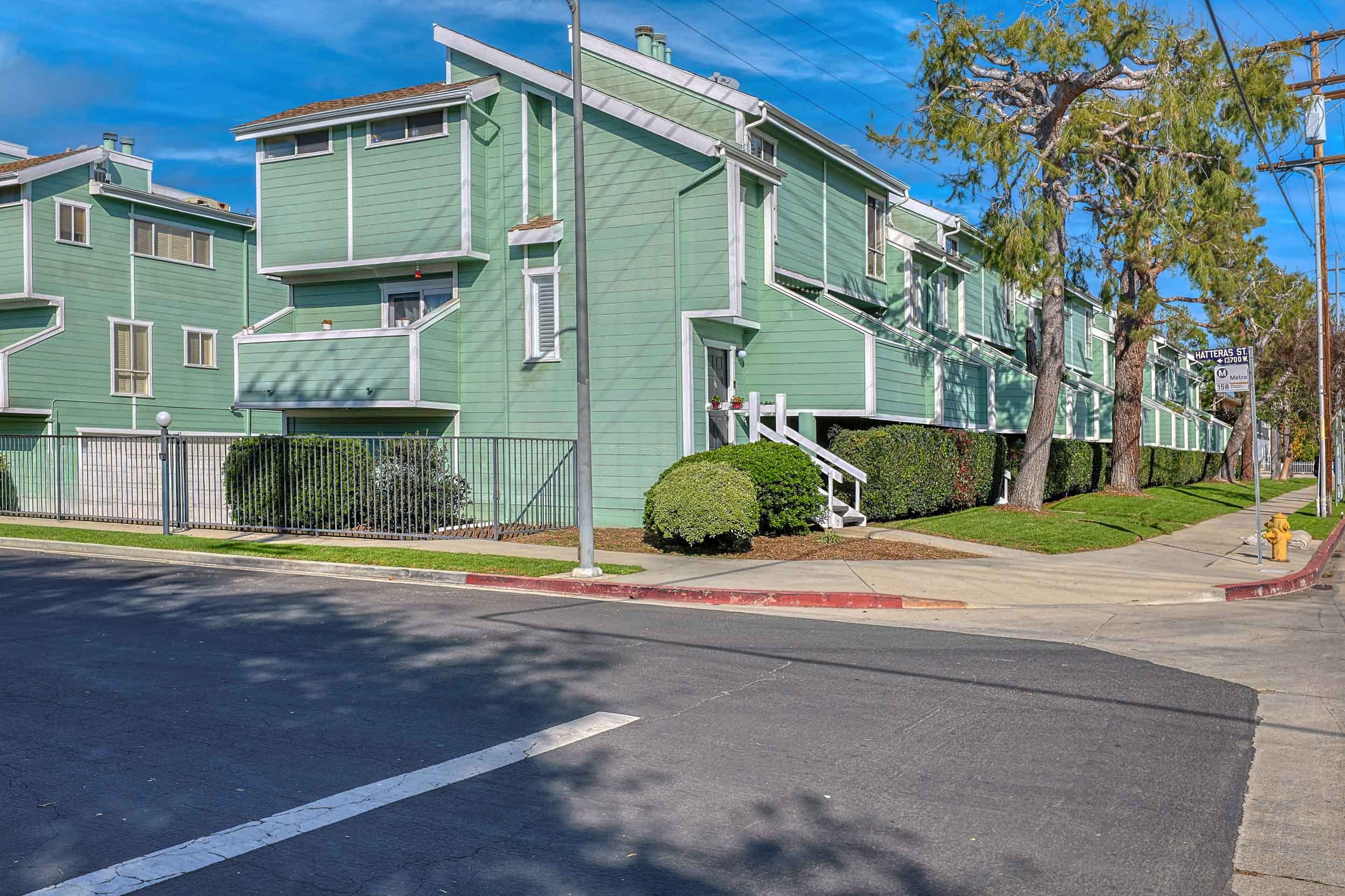 Professional real estate photo of townhome at 5811 Woodman Ave #22, Sherman Oaks, CA 91401 — end-unit exterior with two-car attached garage and Tesla charger.