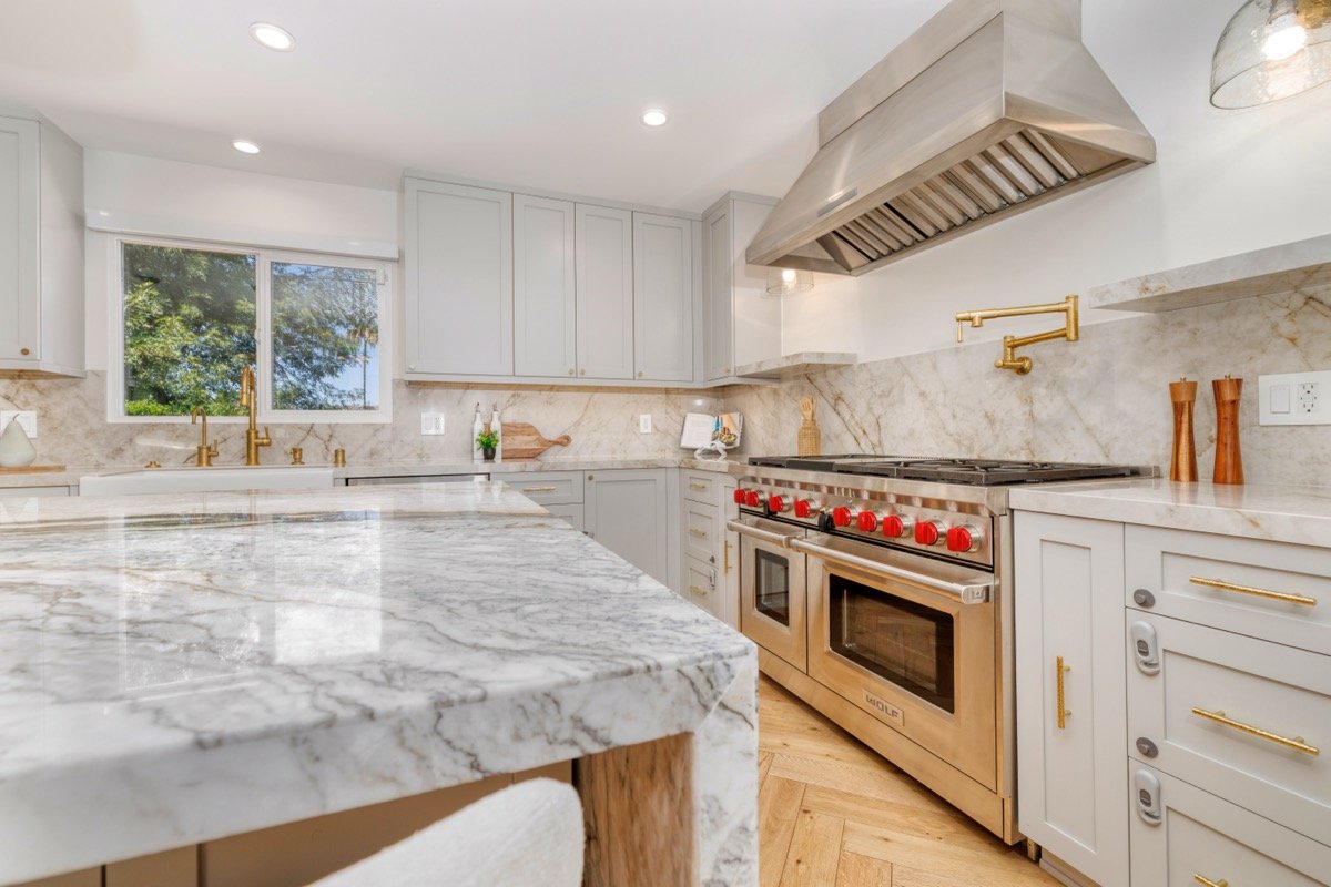 Professional real estate photo of a bright upgraded kitchen with marble countertops Wolf range and gold accents in Woodland Hills