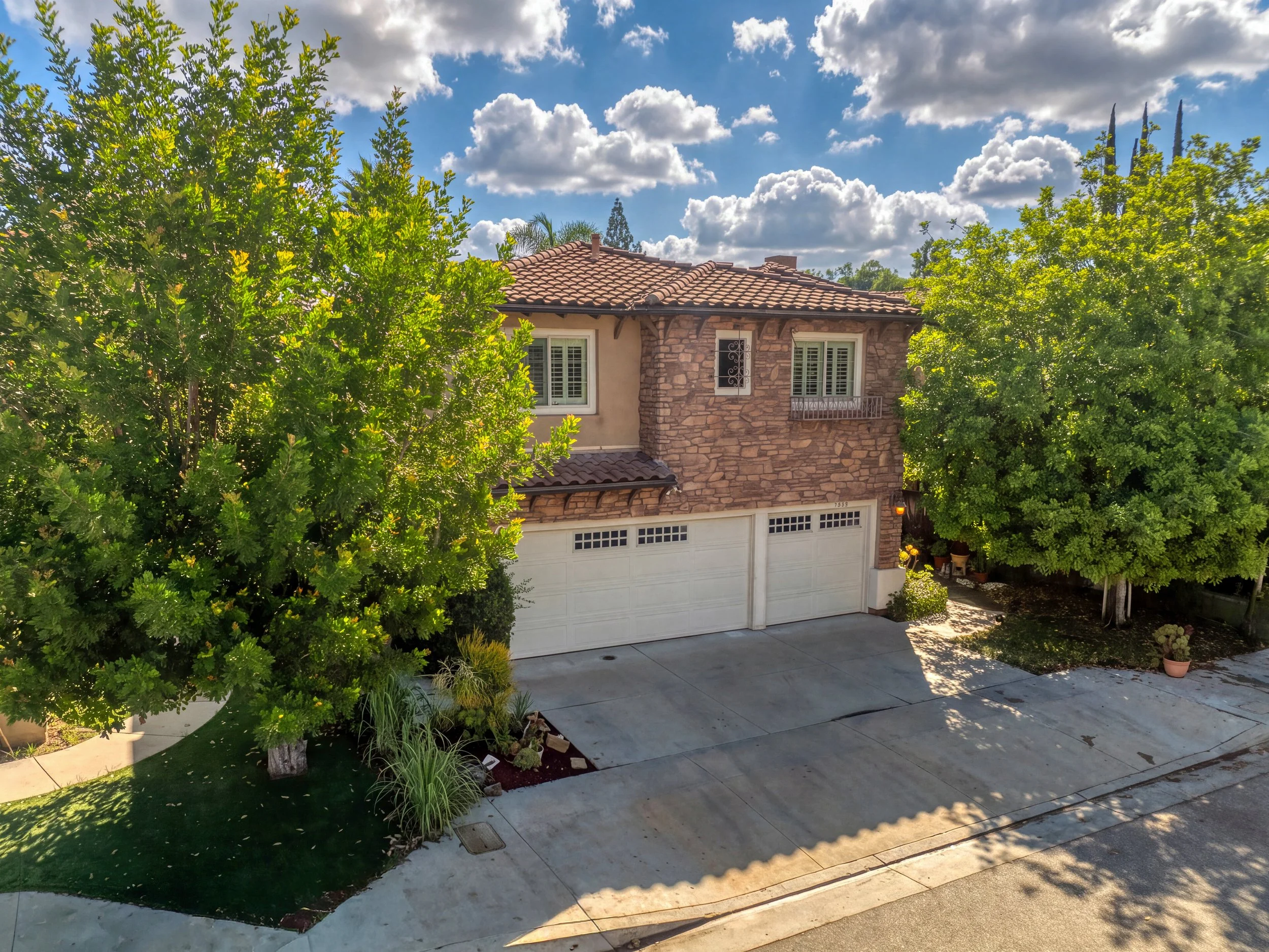 Professional real estate photo of West Hills home with stone facade, tile roof, white garage doors, and leafy trees