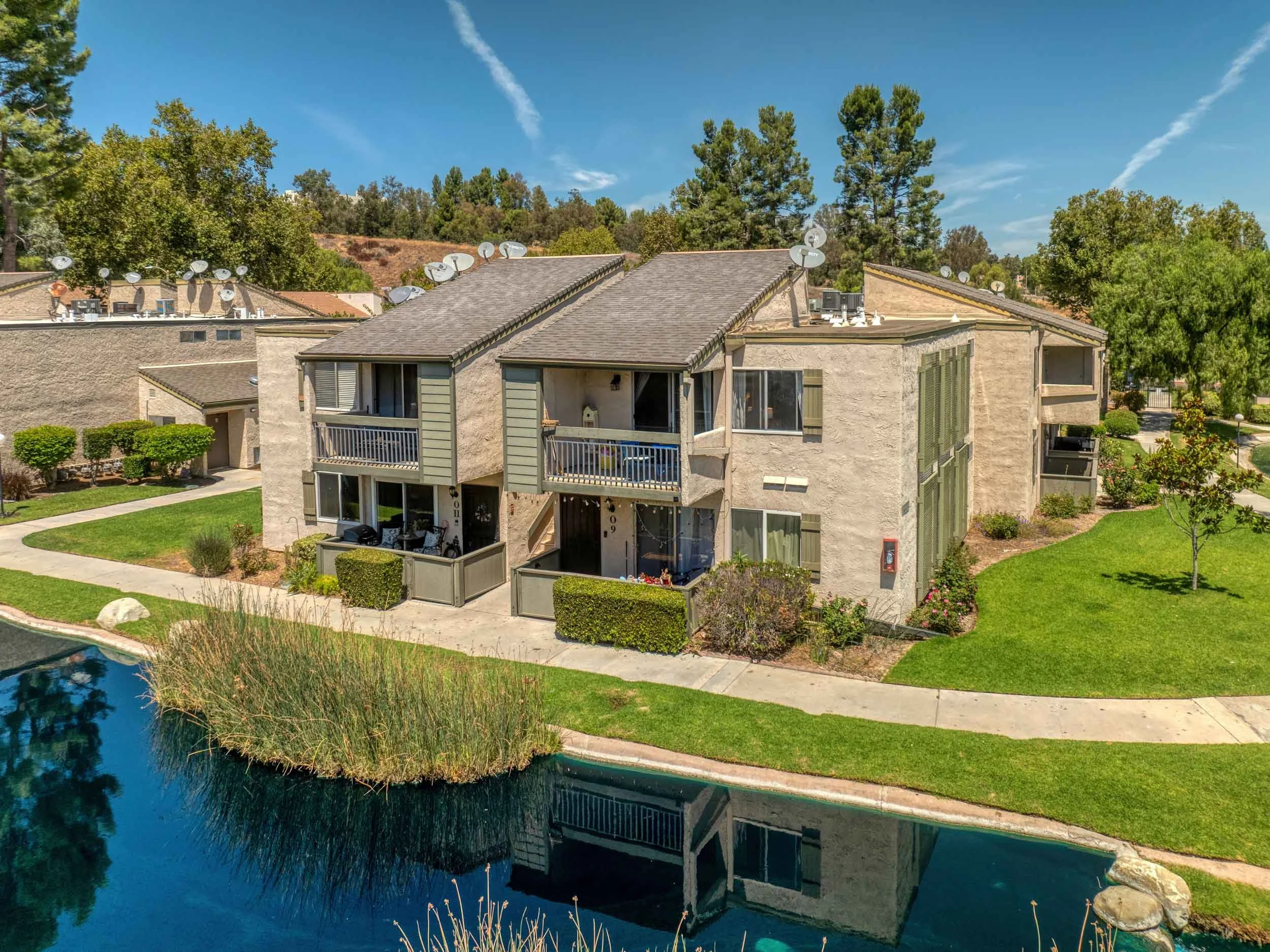 Professional real estate photo of a lakefront Valencia condo with lush landscaping, balconies, and a serene pond reflection