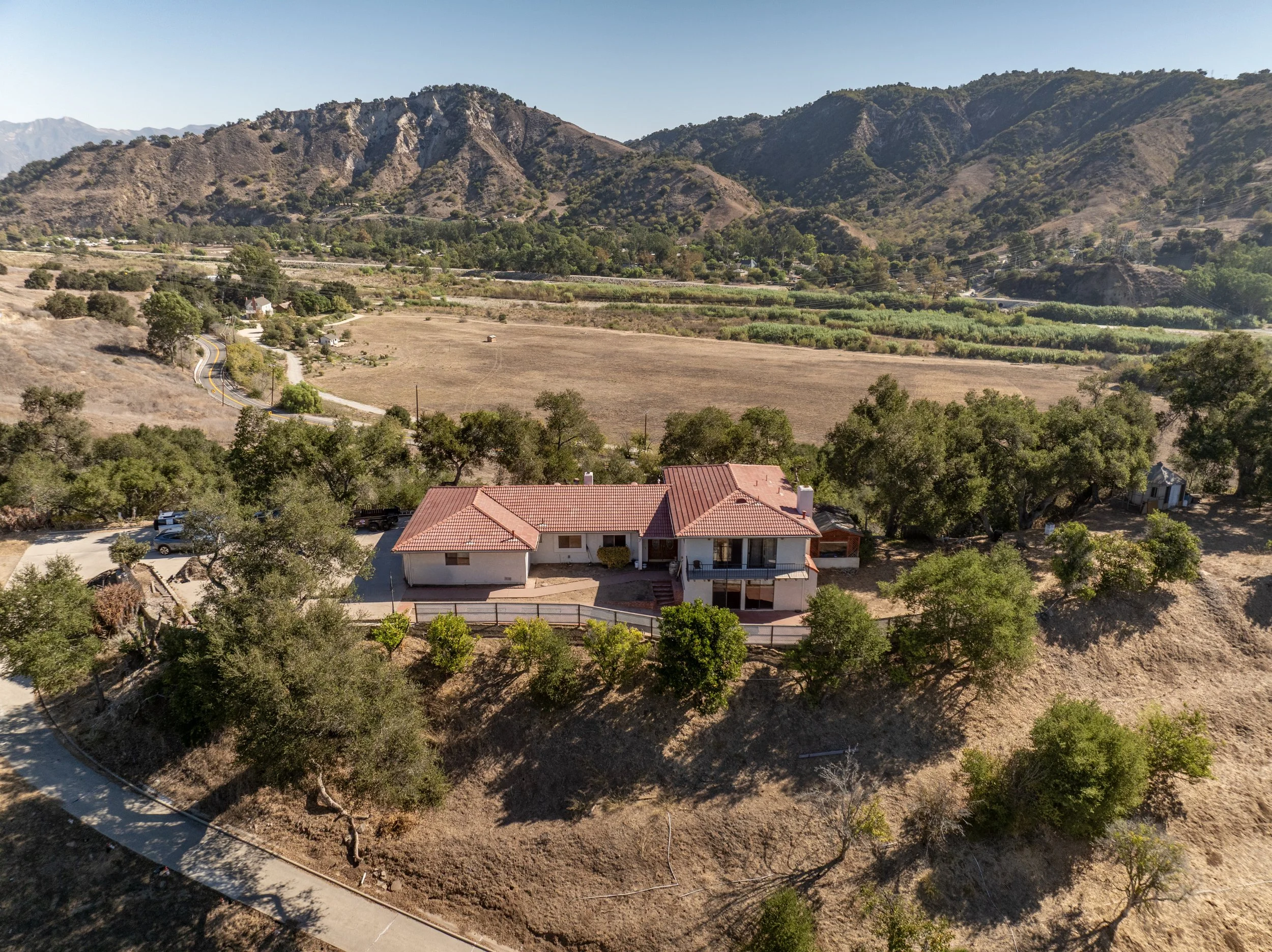 Professional real estate photo of a Ventura home with red tile roofing, surrounding trees, and rugged mountain ridges.