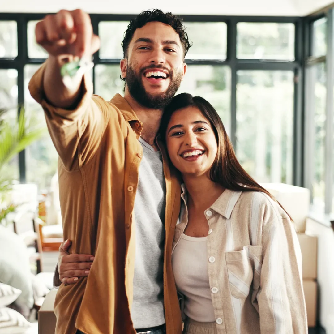 Two smiling friends, a man and a woman, taking a selfie together inside a bright room with large windows.