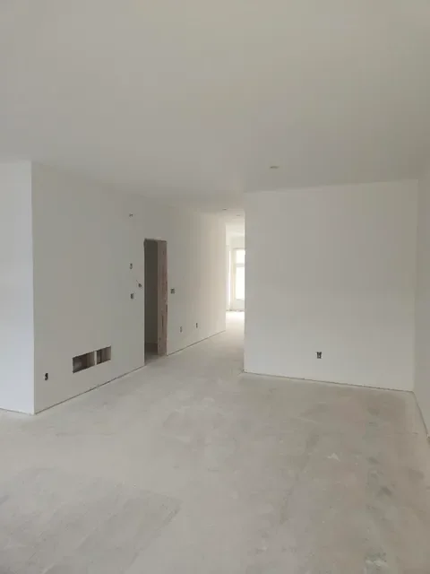 Empty, unfurnished room with white walls and unfinished flooring in a new building.