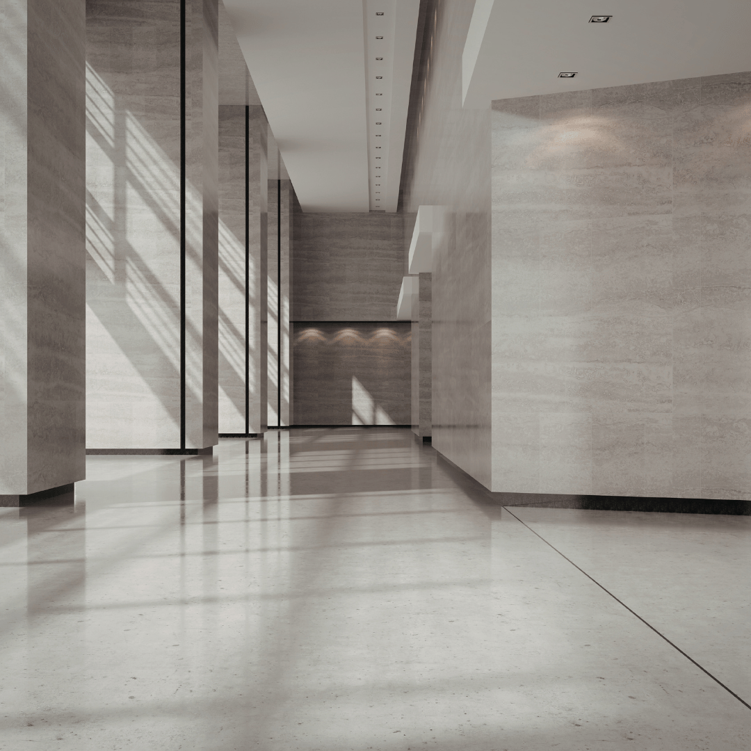 Interior view of a modern building with light-colored marble walls and floors, and sunlight streaming through large windows, creating shadows on the floor.