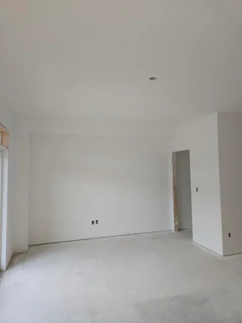 Empty room with white walls, some electrical outlets, and a doorway under construction.