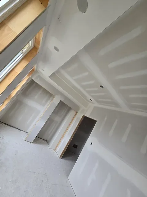 Interior of a room under construction with drywall installation, visible drywall seams, and unfinished ceiling.