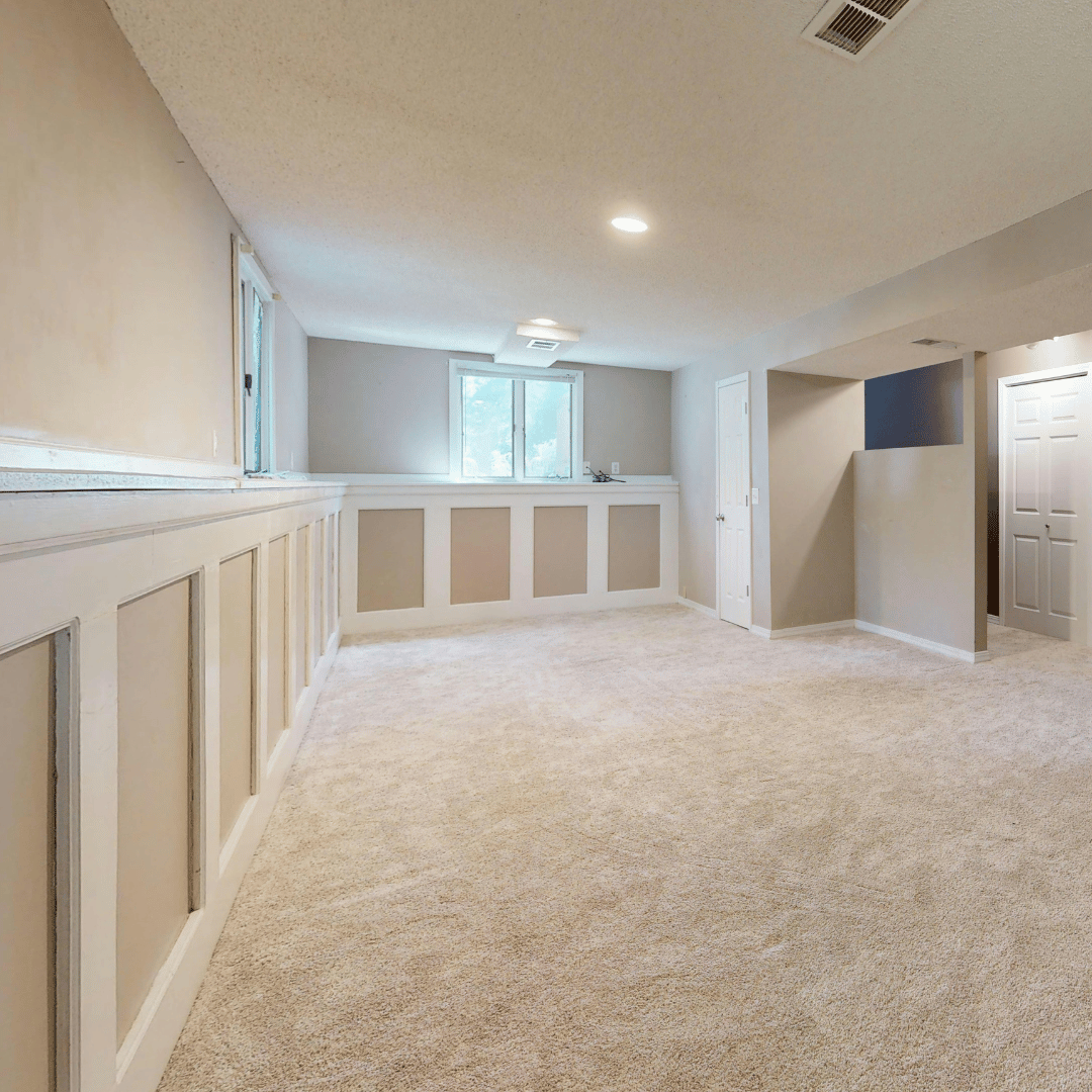 Empty finished basement with beige walls, carpeted floor, and a window