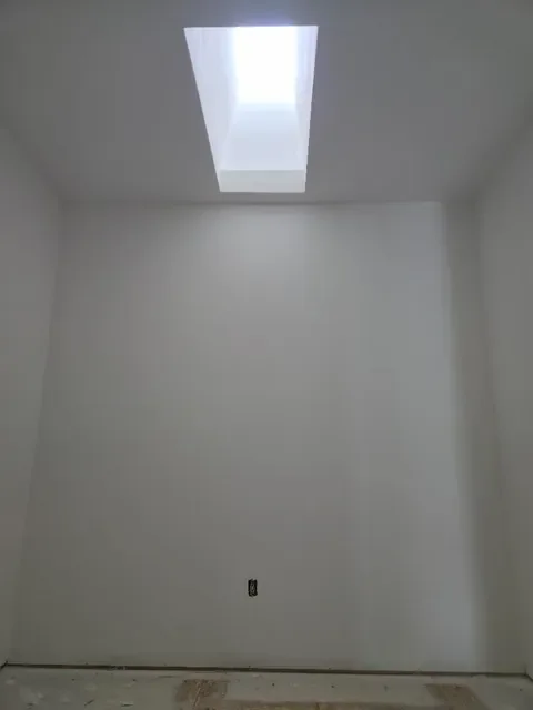 Empty room with a skylight window at the top, plain white walls, and an electrical outlet on the wall near the floor.