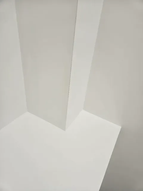 Close-up of a corner where a vertical white wall meets a white baseboard and white floor.