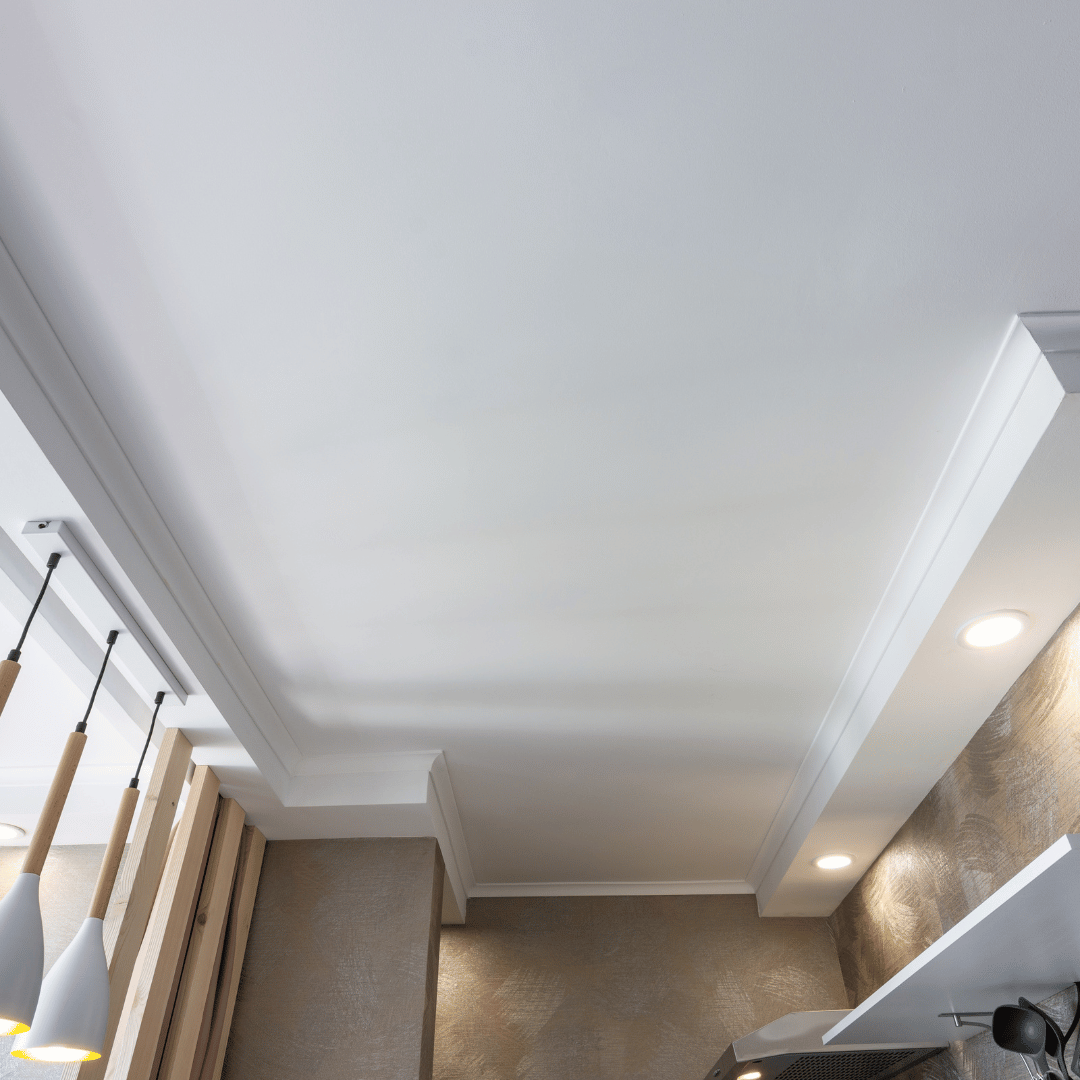 Ceiling with recessed lights, crown molding, and part of a kitchen area with pendant lights and a textured wall.