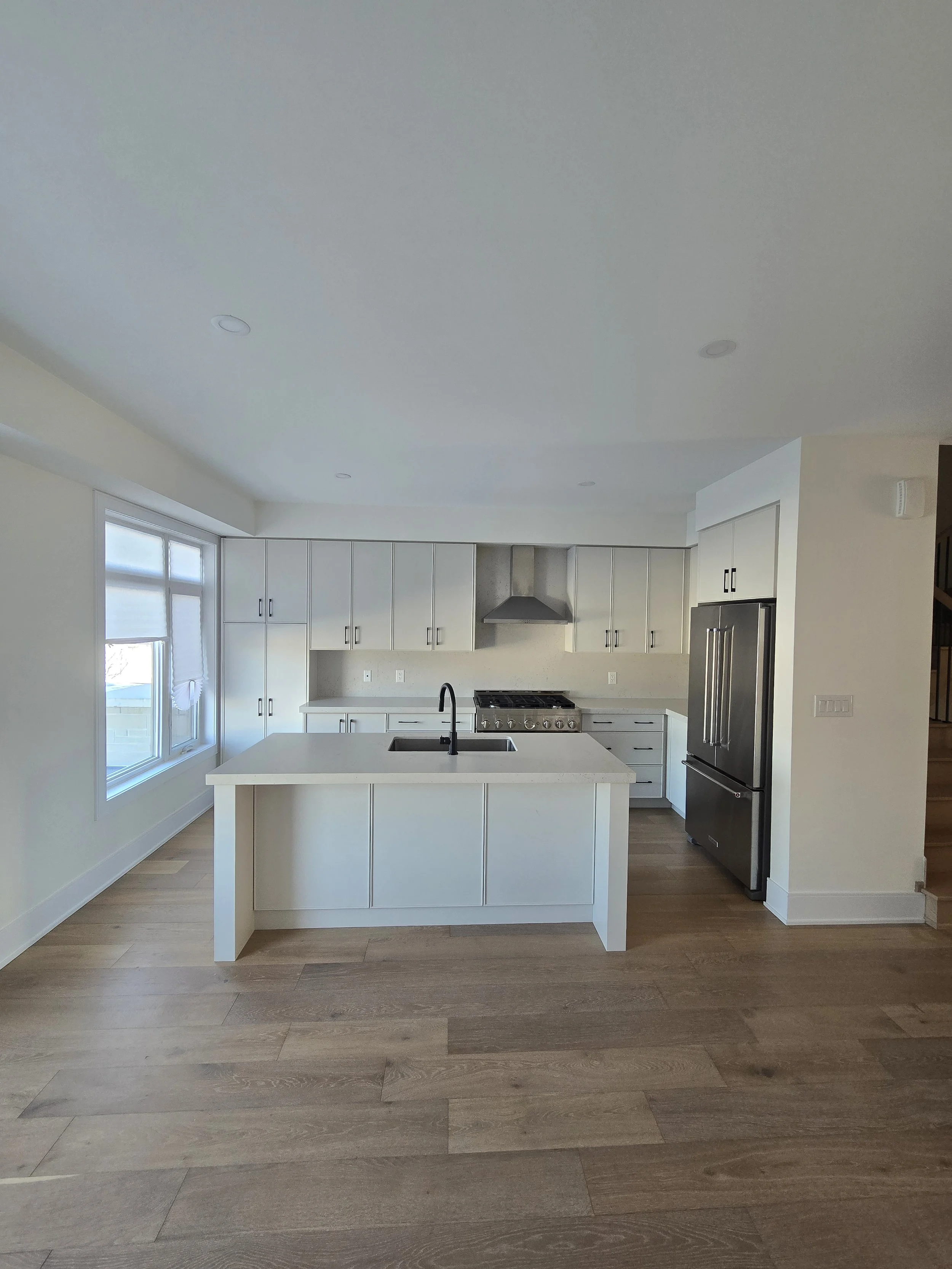 Modern kitchen with white cabinets, a large kitchen island with a sink, stainless steel appliances including a refrigerator, and wood flooring.