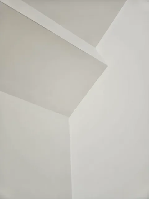 Close-up of a ceiling corner with white walls and an angled ceiling.