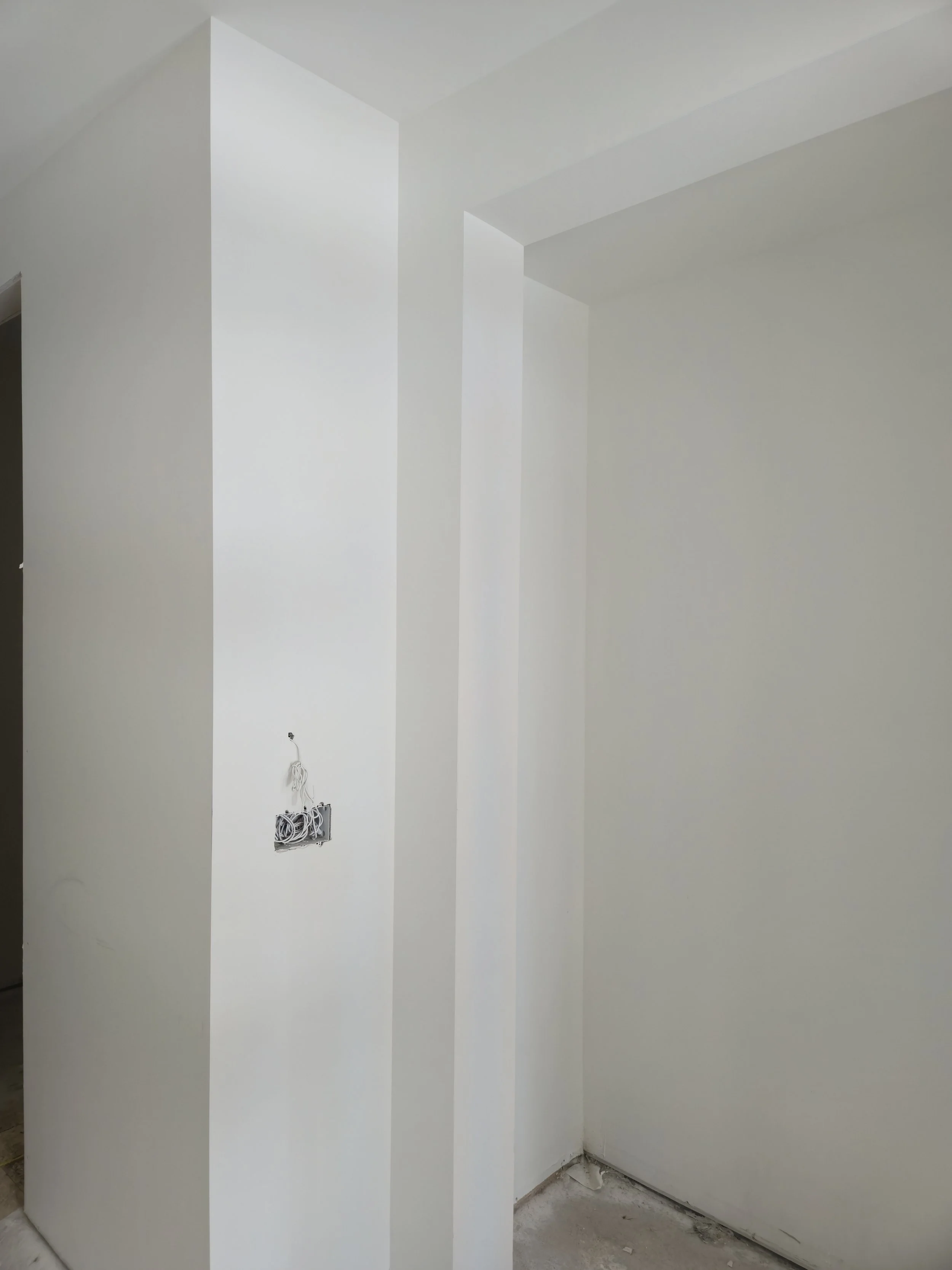 Interior of a room under construction with white walls, an electrical outlet box without cover, and exposed wiring.