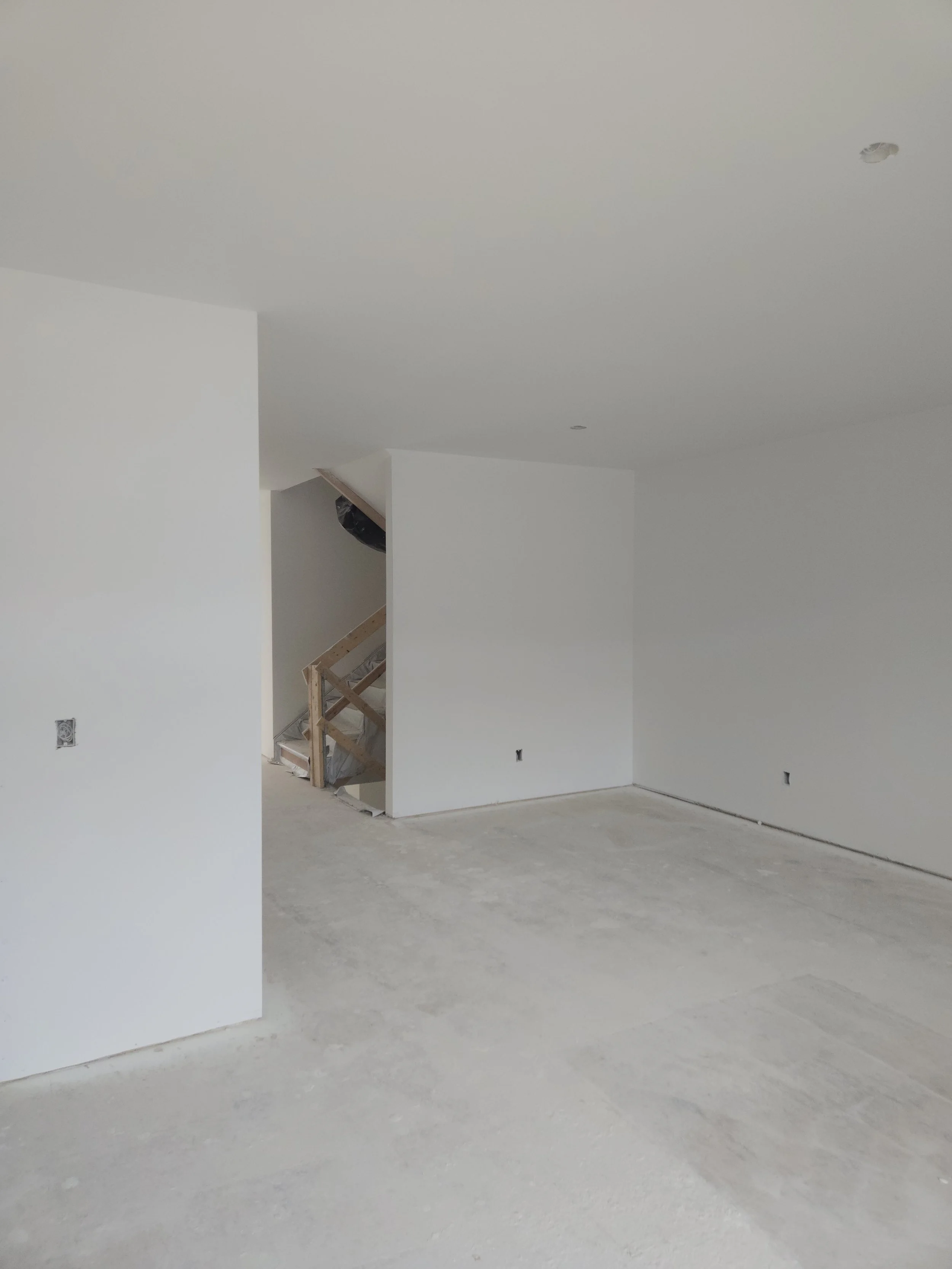 Empty room under construction with white walls, unfinished concrete floor, and a staircase framed with wood near the wall.