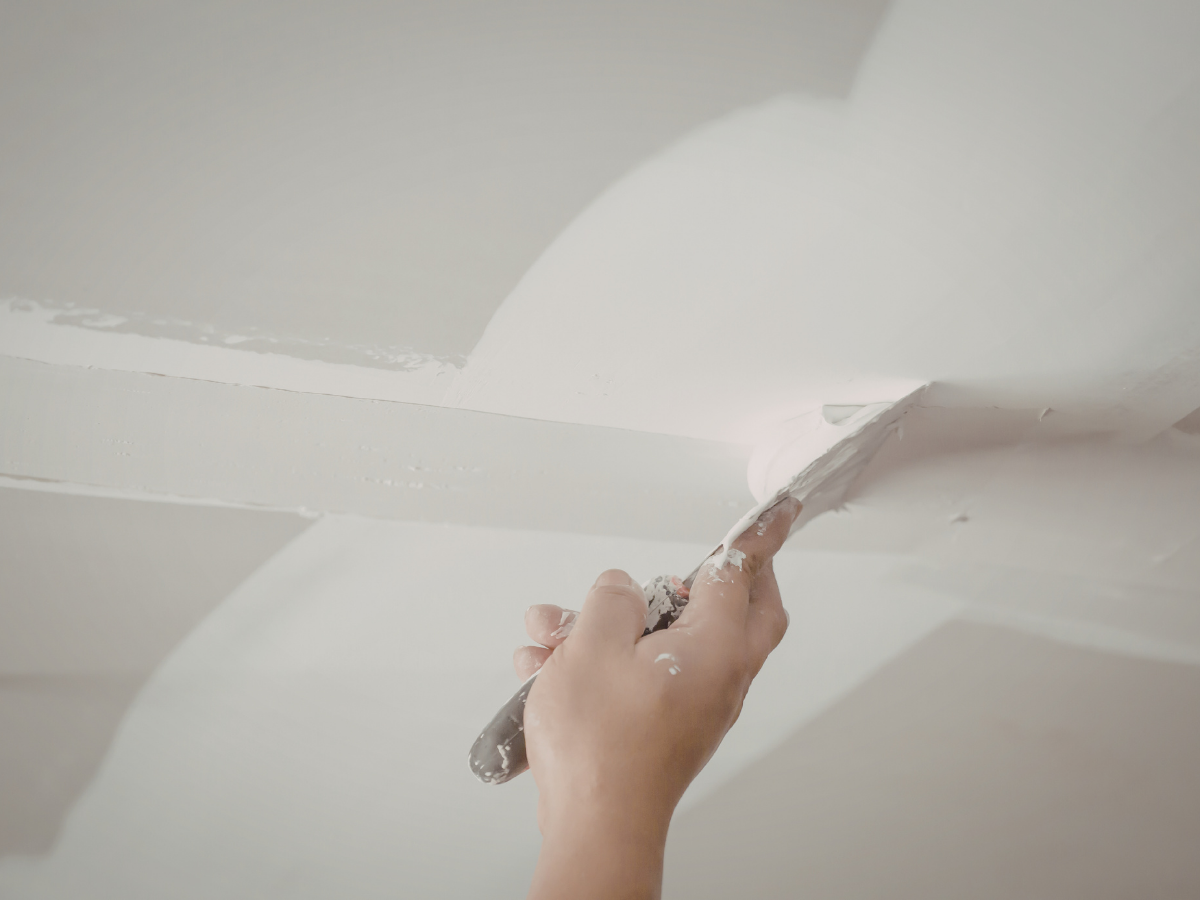 Person applying white paint on ceiling with a paint spatula.