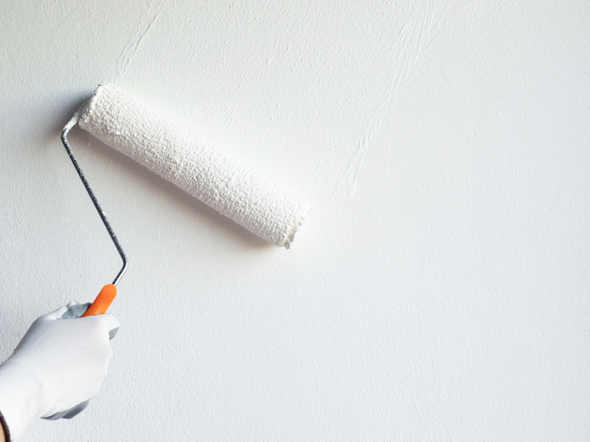 A paint roller covered in white paint being used to paint a white wall.