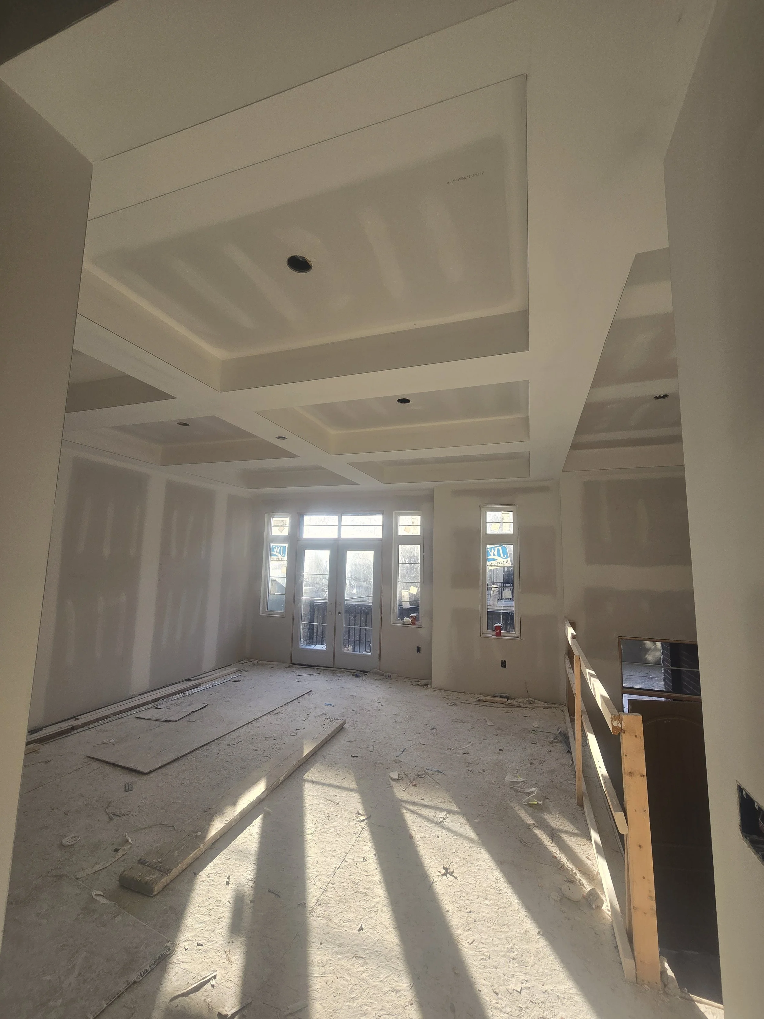 Room under construction with drywall, uninstalled flooring, and sunlight coming through windows.
