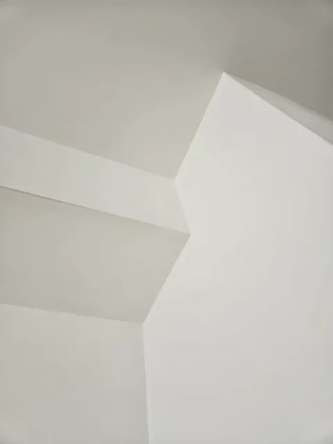 Close-up of a white ceiling corner with a partial view of a sloped ceiling and a white wall.