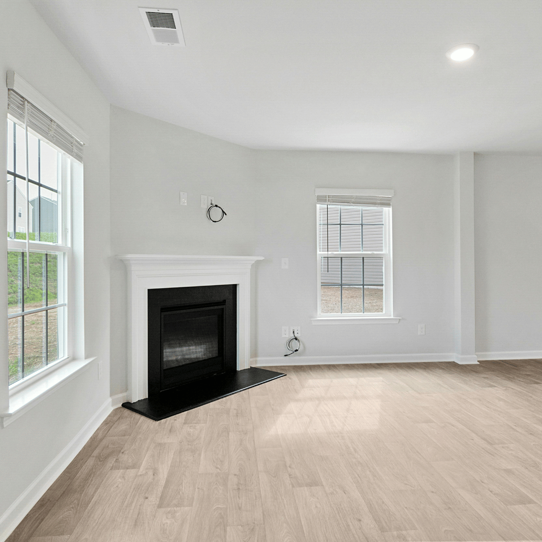 Empty living room with a fireplace, light wood floors, and large windows with white blinds.