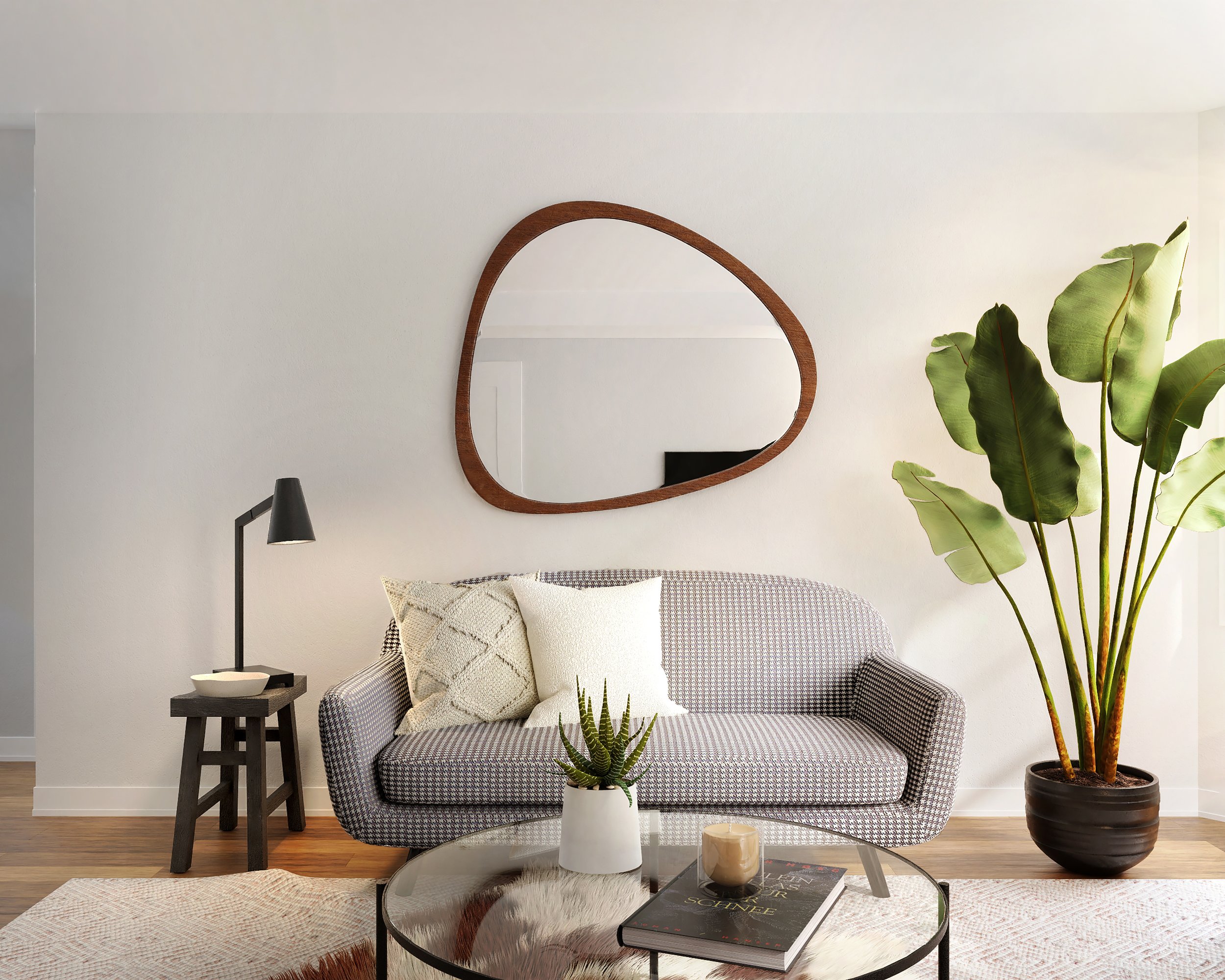 Living room with a patterned sofa, set of pillows, a round glass coffee table with books and decor, a potted plant, wall mirror, and a floor lamp.
