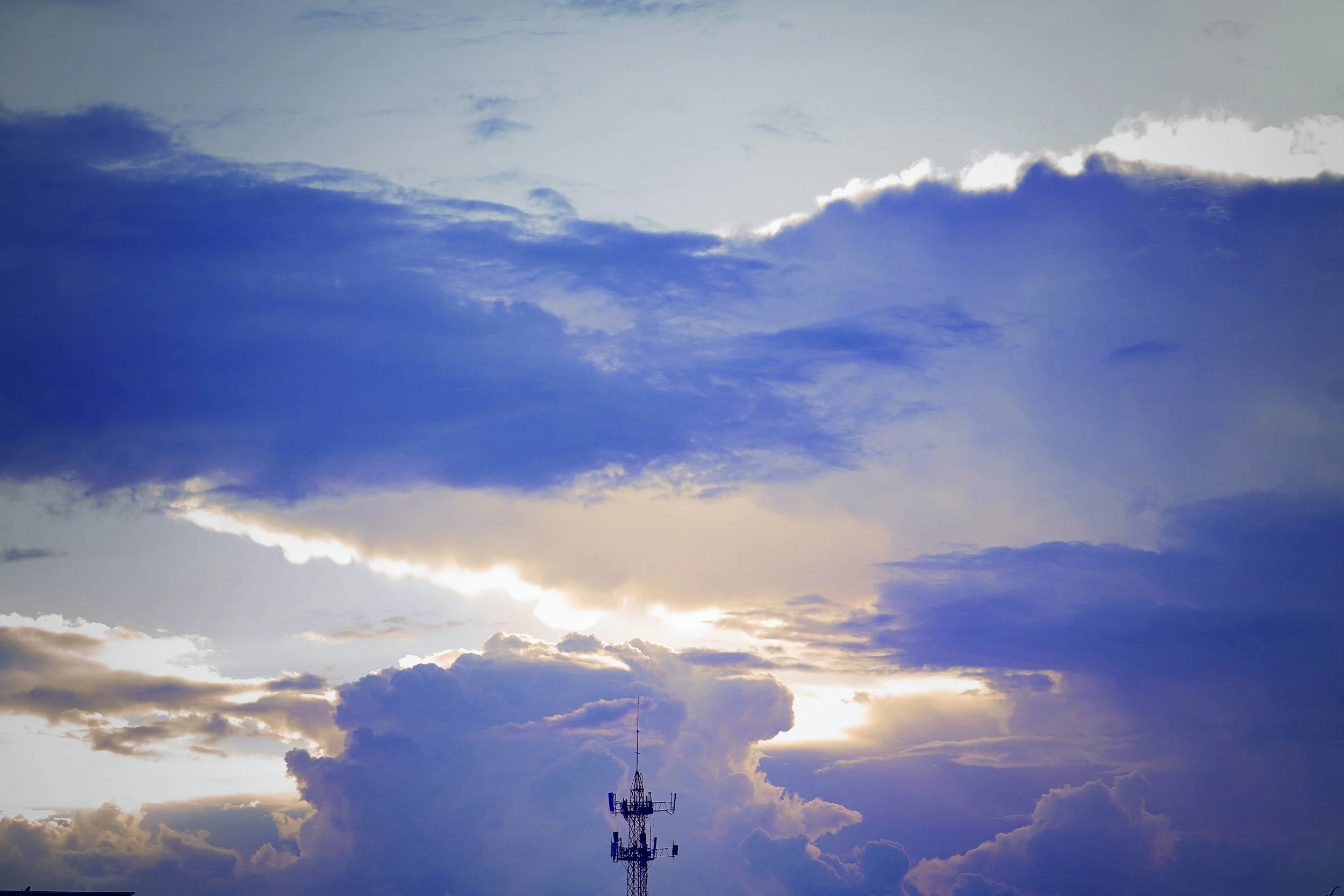 Sky with clouds and sunlight, with a radio tower at the bottom.