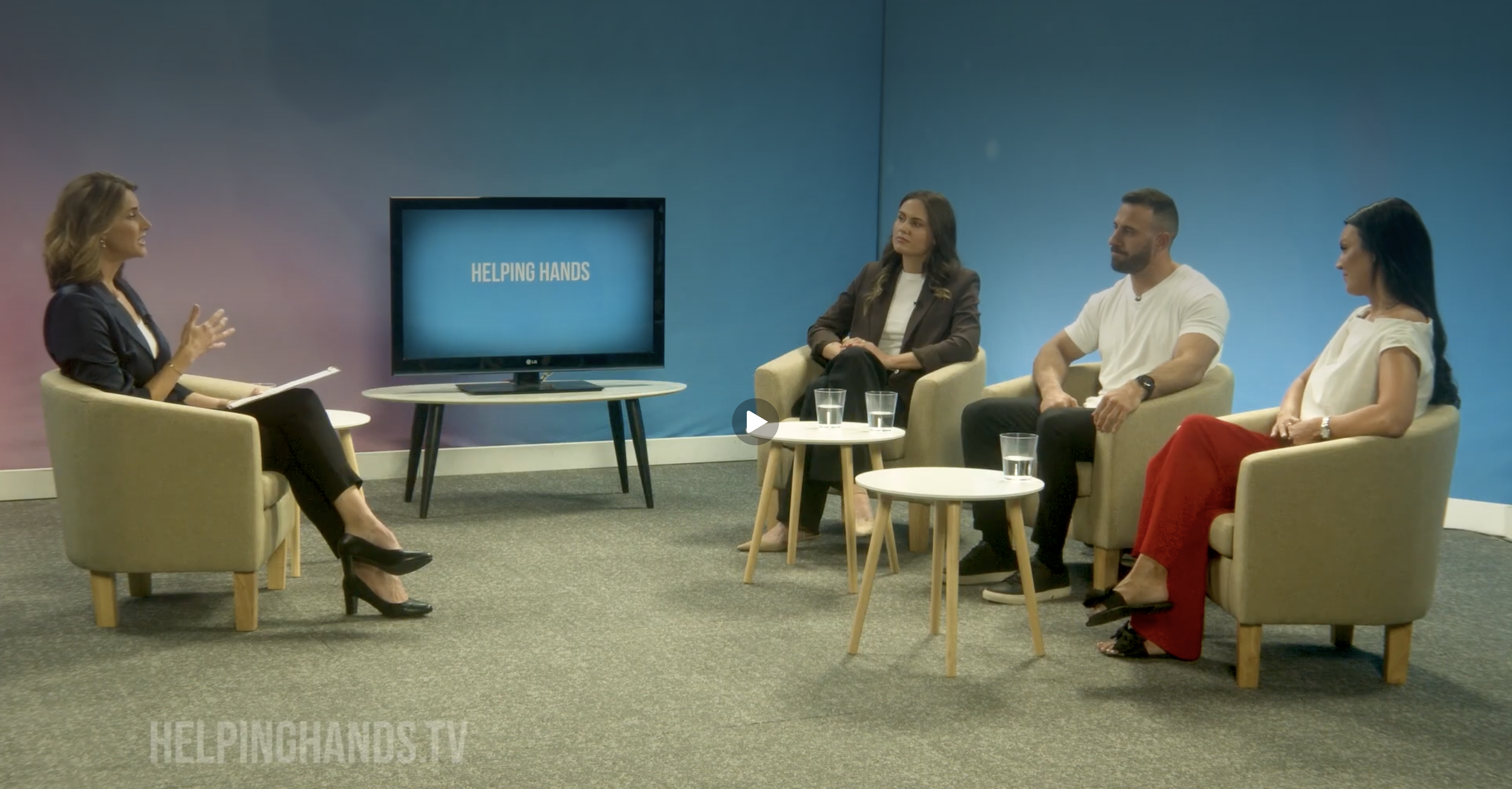 Dave Kramer in a group of three other people sitting in chairs during a panel discussion, with a woman on the left speaking, and a screen behind her displaying 'Helping Hands'.