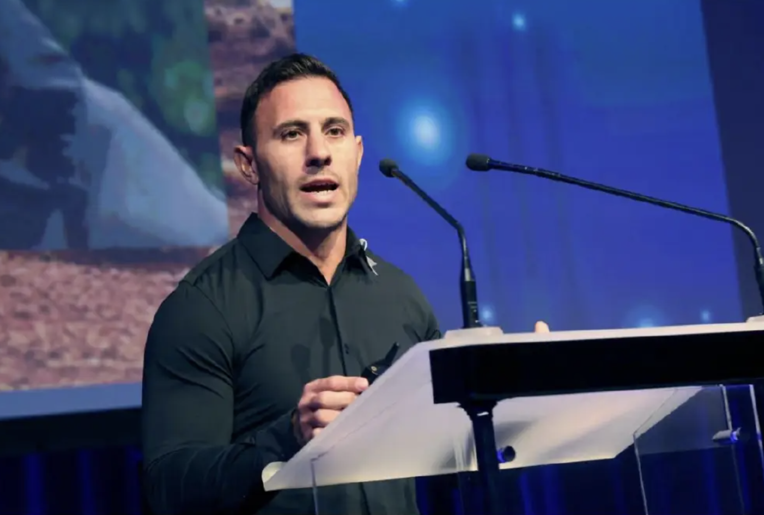 Dave Kramer is speaking at a podium during a conference or presentation, with a large screen displaying an image behind him.