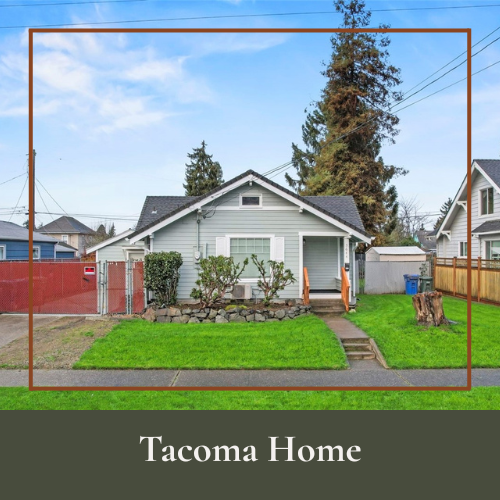 A light blue house with a small front porch, surrounded by a green lawn and trees, with neighboring houses visible, under a partly cloudy sky.